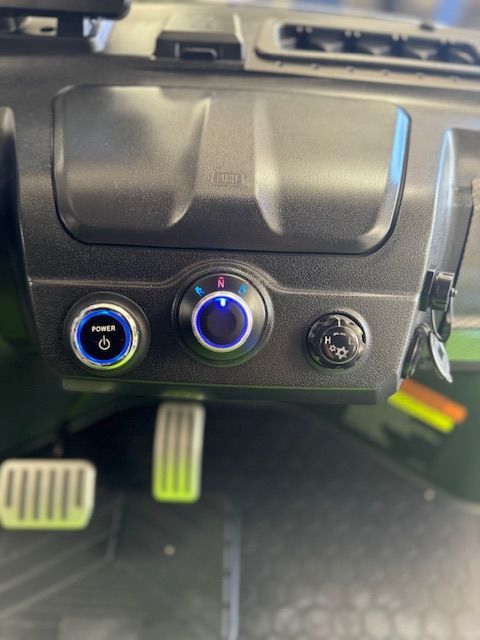 Dashboard controls featuring power, drive mode, and a knob, illuminated in blue, with pedals in the foreground.