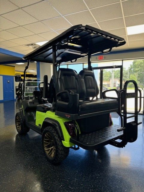 Green and black custom golf cart with a black roof, parked indoors.  It has black seats, bronze wheels, and a rear platform.