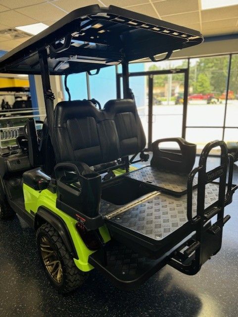 Green and black golf cart with a cargo bed, black seats, and a sunshade, indoors.