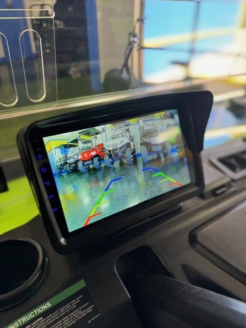 Backup camera screen in a vehicle, showing a red ATV and parking guidance lines.  Black screen with a sun visor is mounted on a dashboard.