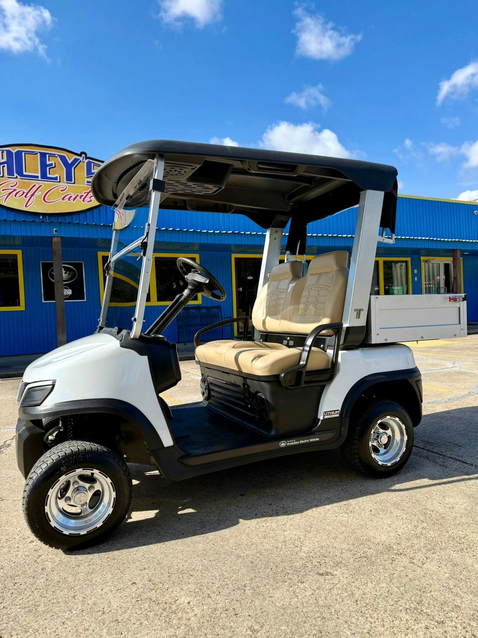 White golf cart with black accents, parked on gravel in front of a blue building with sign.