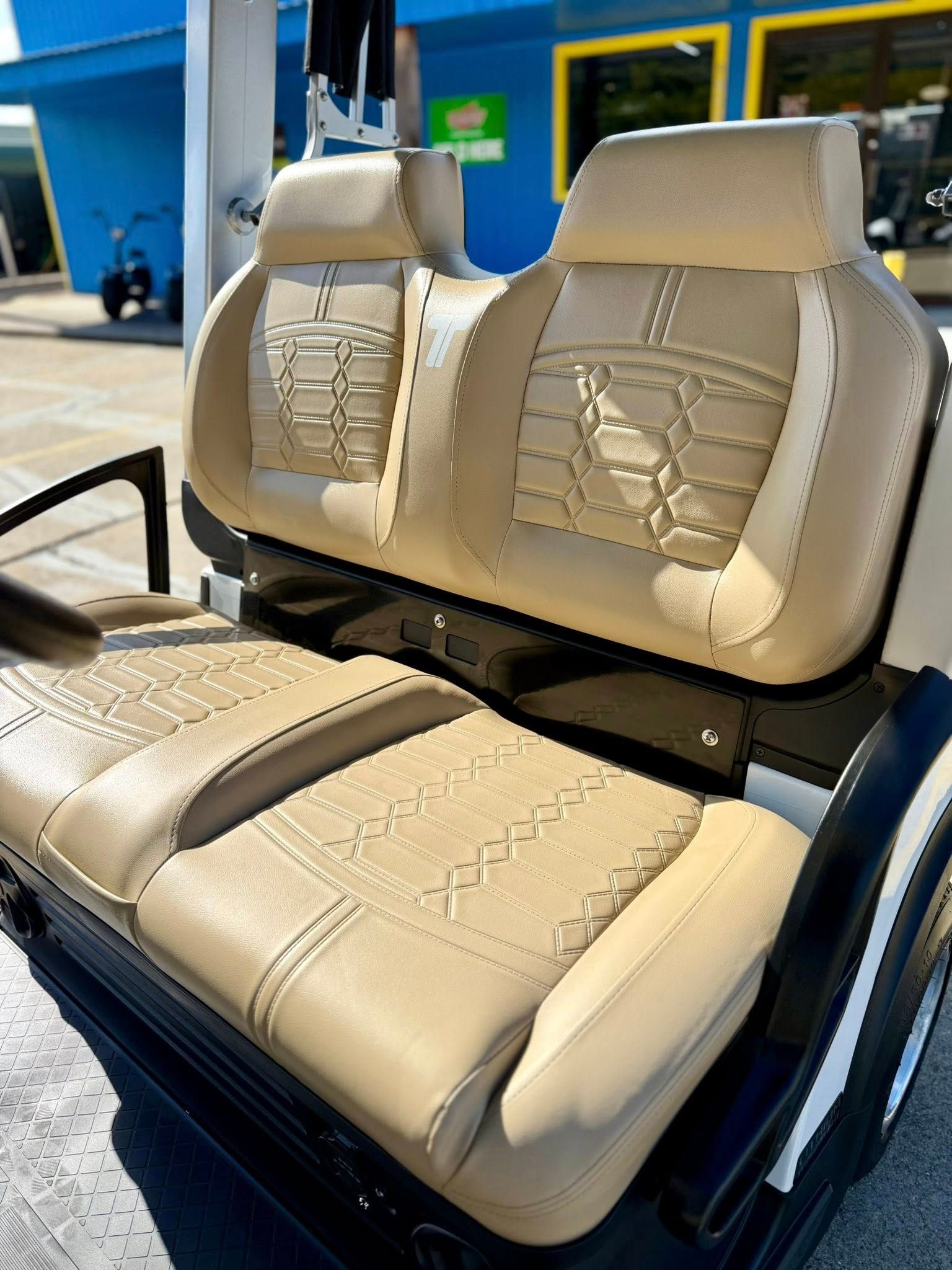 Tan golf cart seats with decorative stitching, parked outside a building.