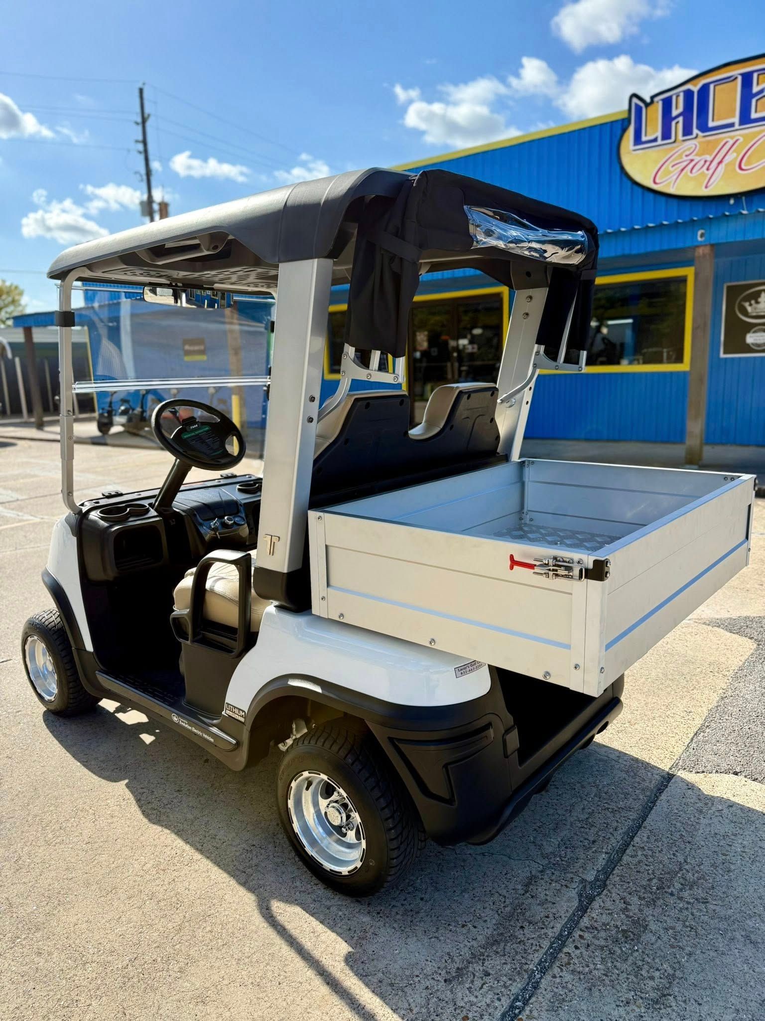 White utility golf cart with a cargo bed, parked on a sunny day.