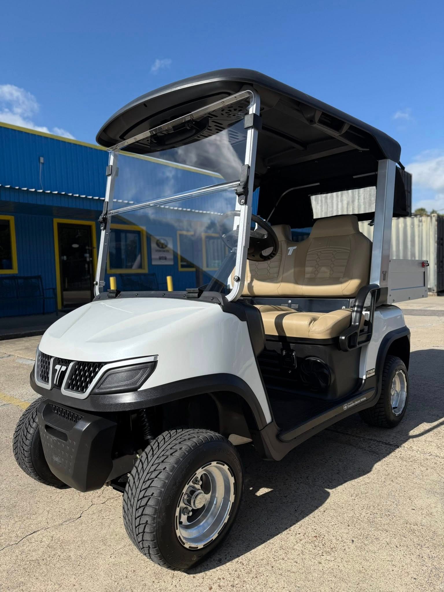 White golf cart with black roof, windshield, and off-road tires, parked outdoors.