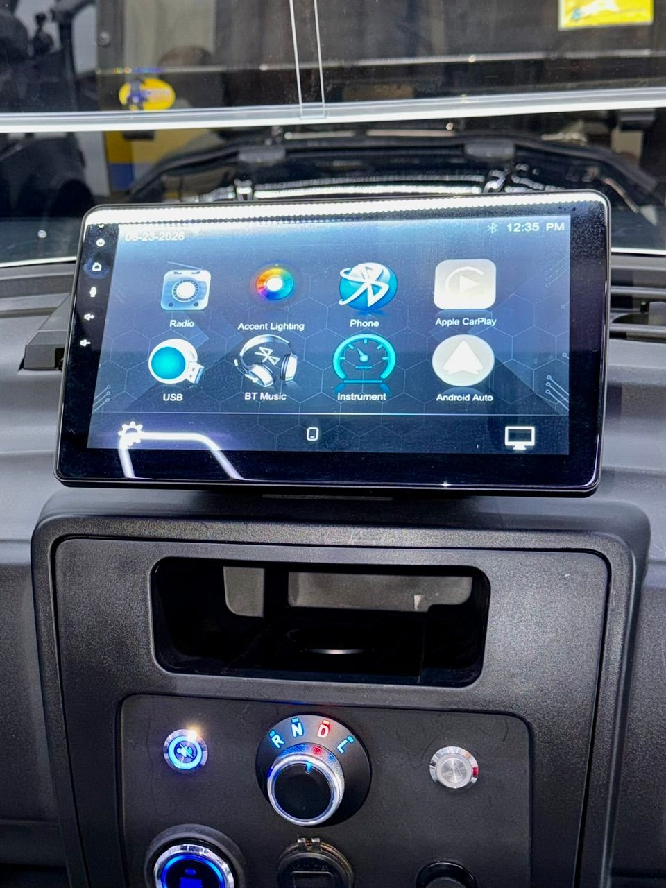 Car dashboard with a touchscreen infotainment display showing app icons and climate controls below.
