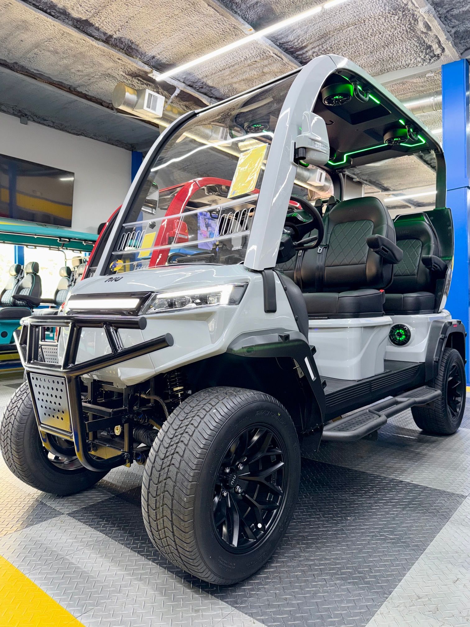 White and black off-road golf cart with lifted tires displayed indoors under bright lights