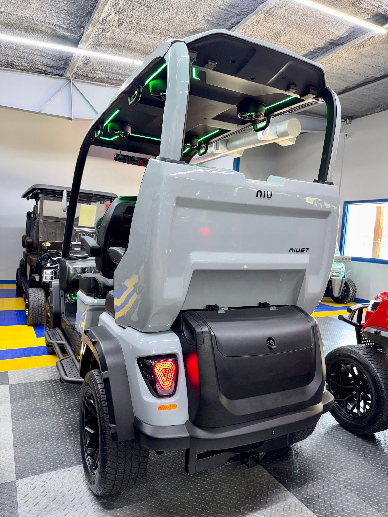 Gray electric golf cart parked indoors on a showroom floor, rear view with black roll cage and taillights.