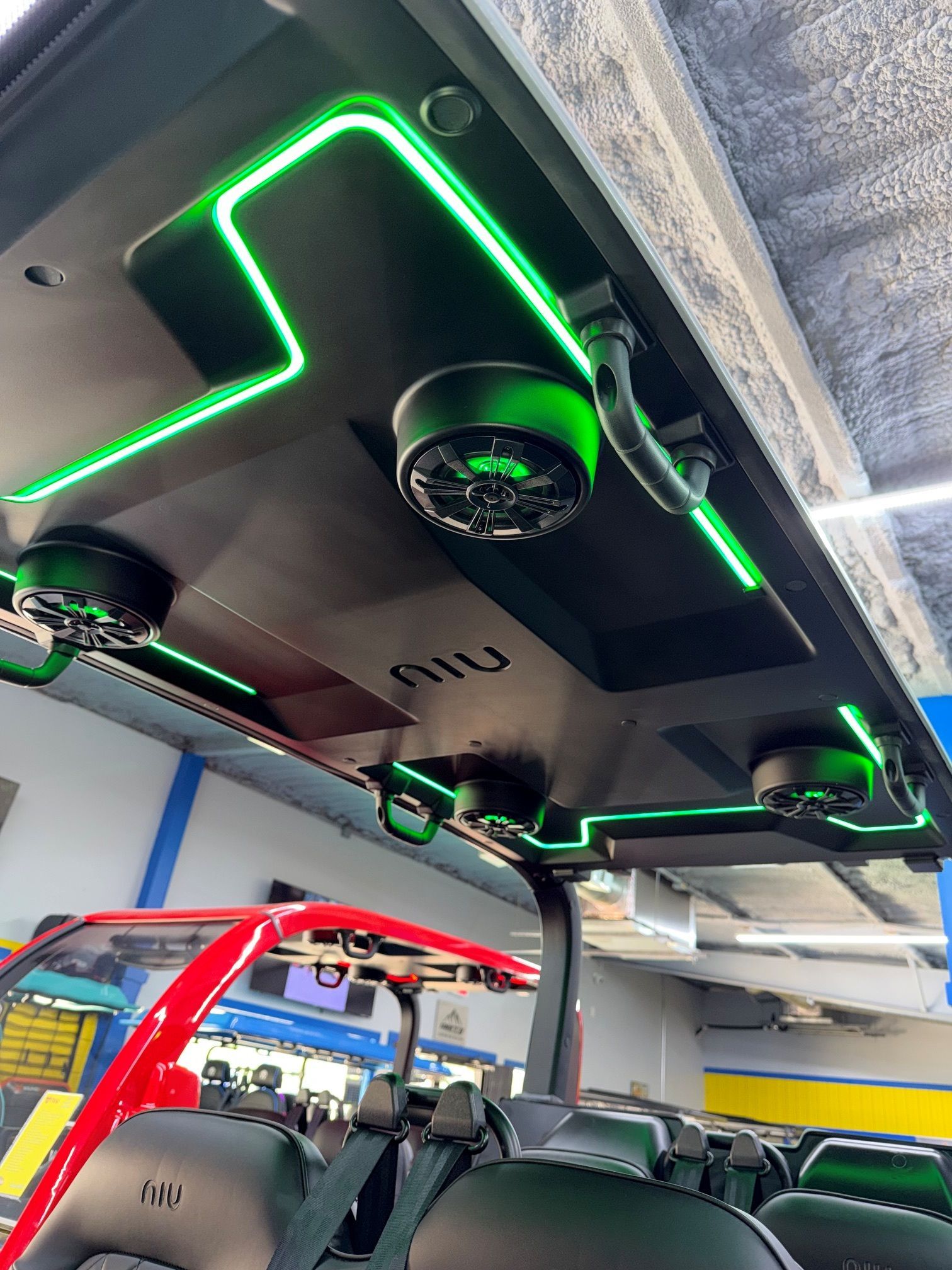 Interior of a vehicle with neon green LED-lit ceiling panels and fans above the seats