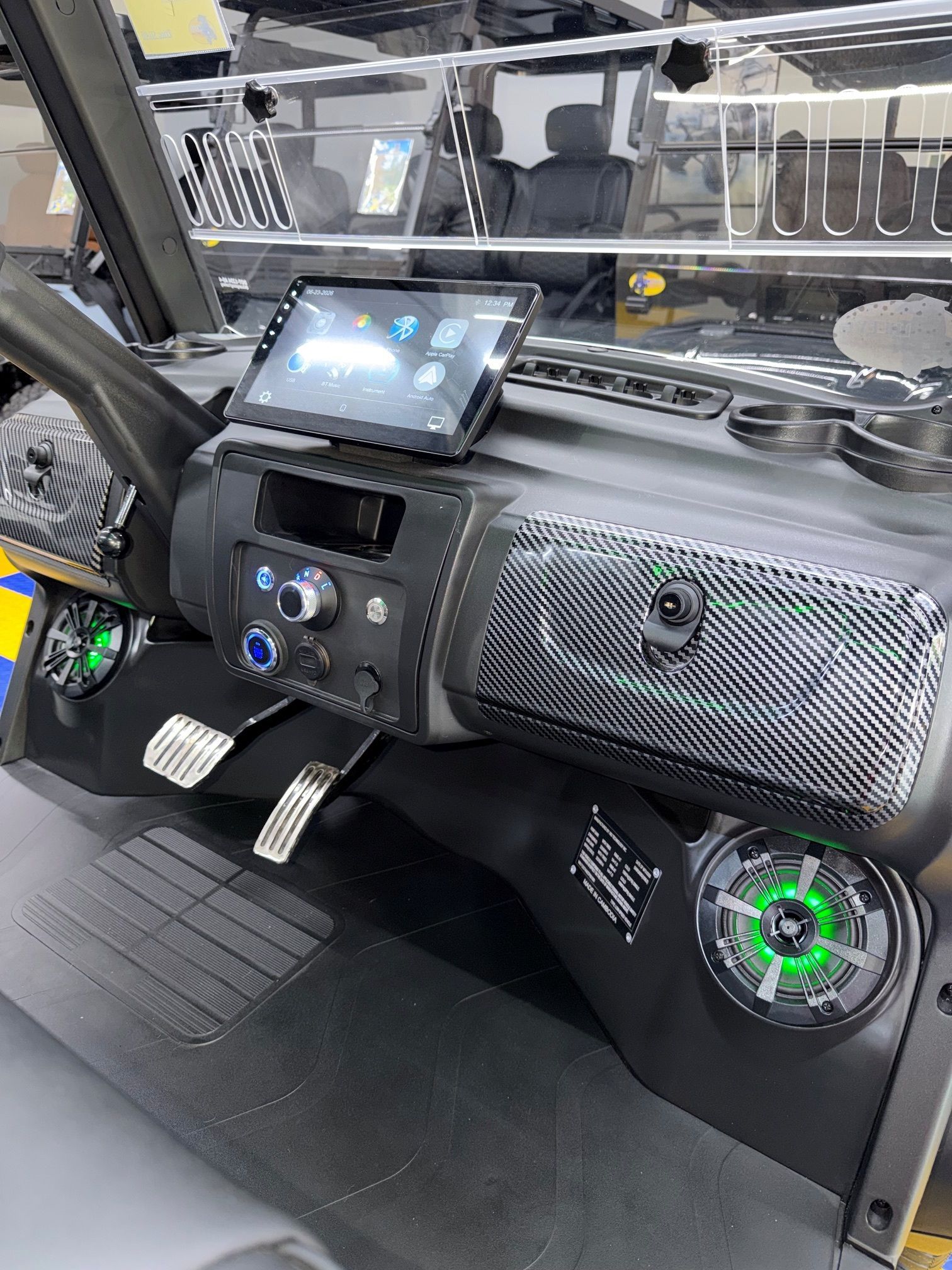 Vehicle interior with touchscreen display, control panel, pedals, and speaker on the passenger side.
