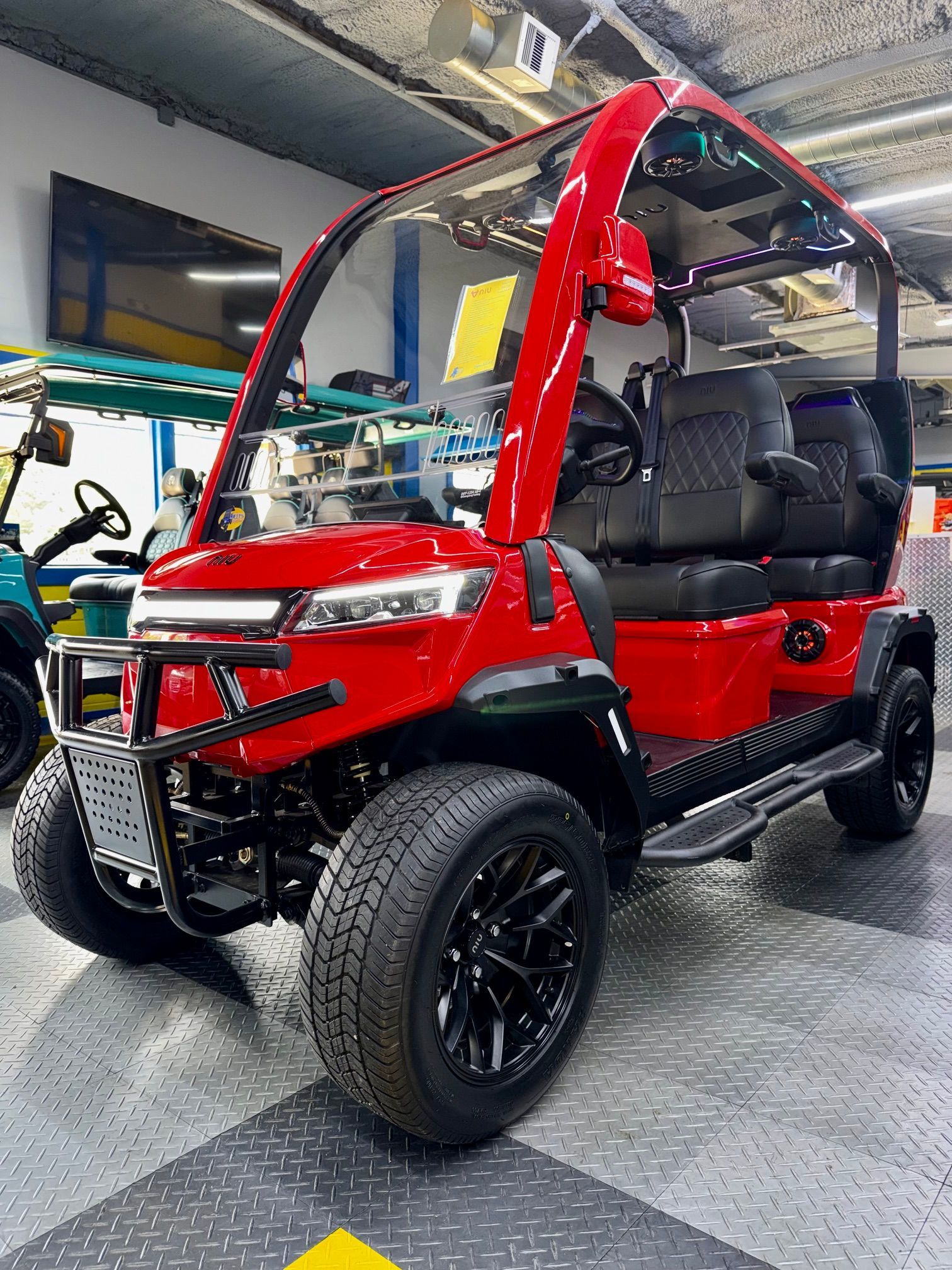 Red and black off-road golf cart with roll cage, parked indoors on a showroom floor.