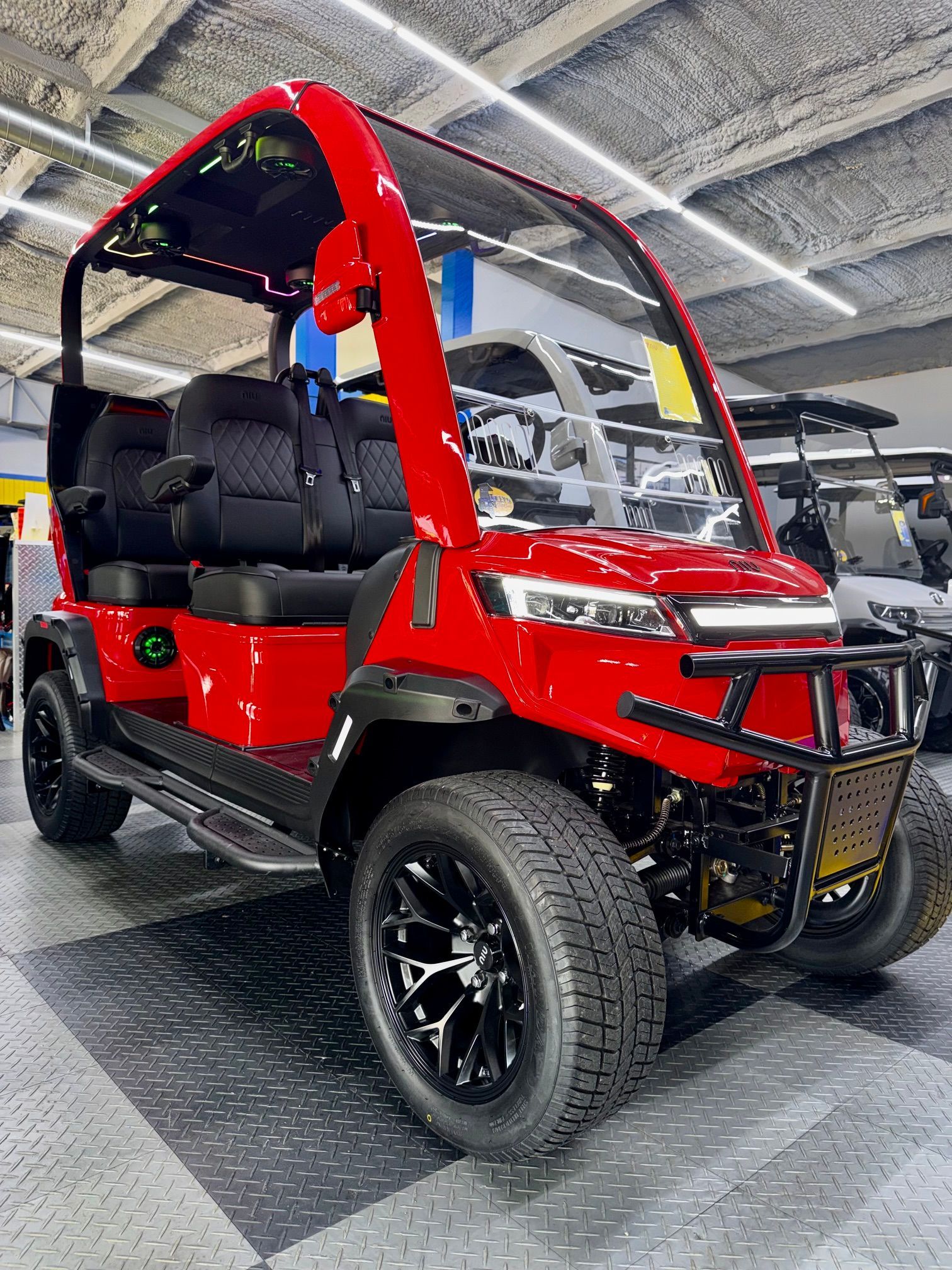 Red off-road utility vehicle with black seats and roll cage, shown indoors on a showroom floor.