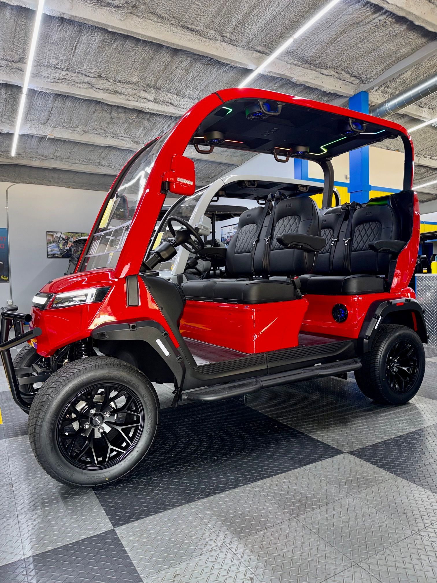 Red electric golf cart with black seats parked indoors on a checkered floor.