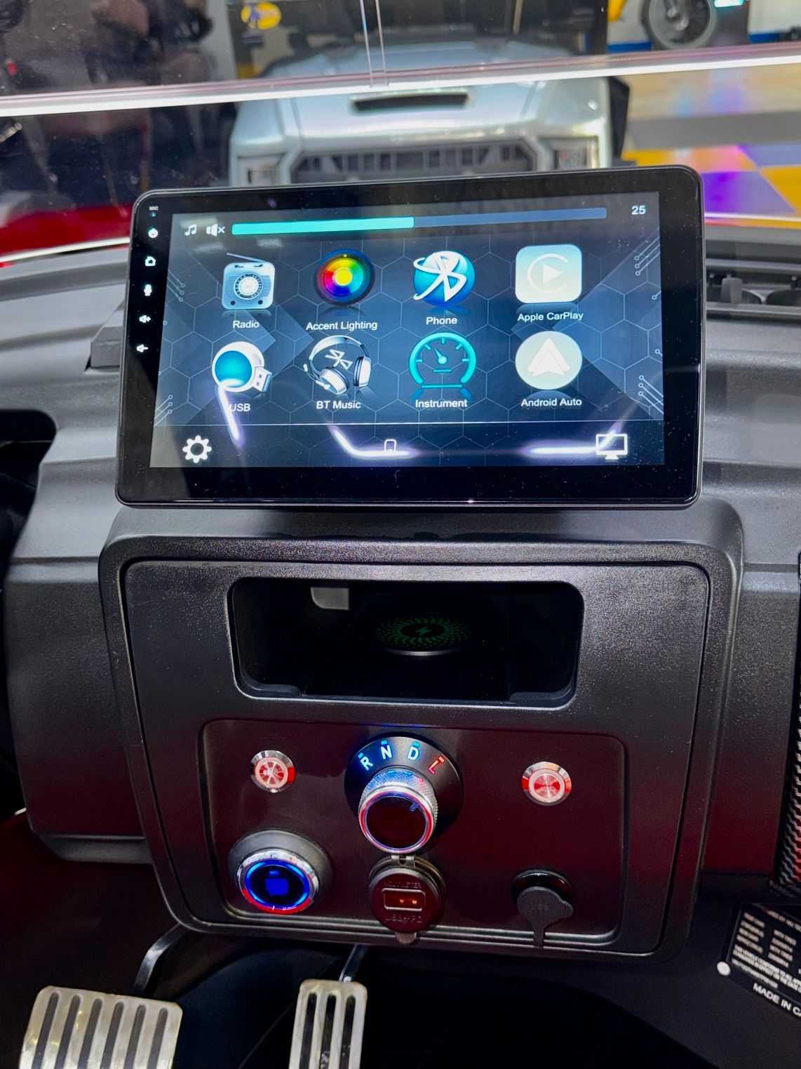 Car dashboard with a touchscreen display showing app icons above climate control knobs and pedals below