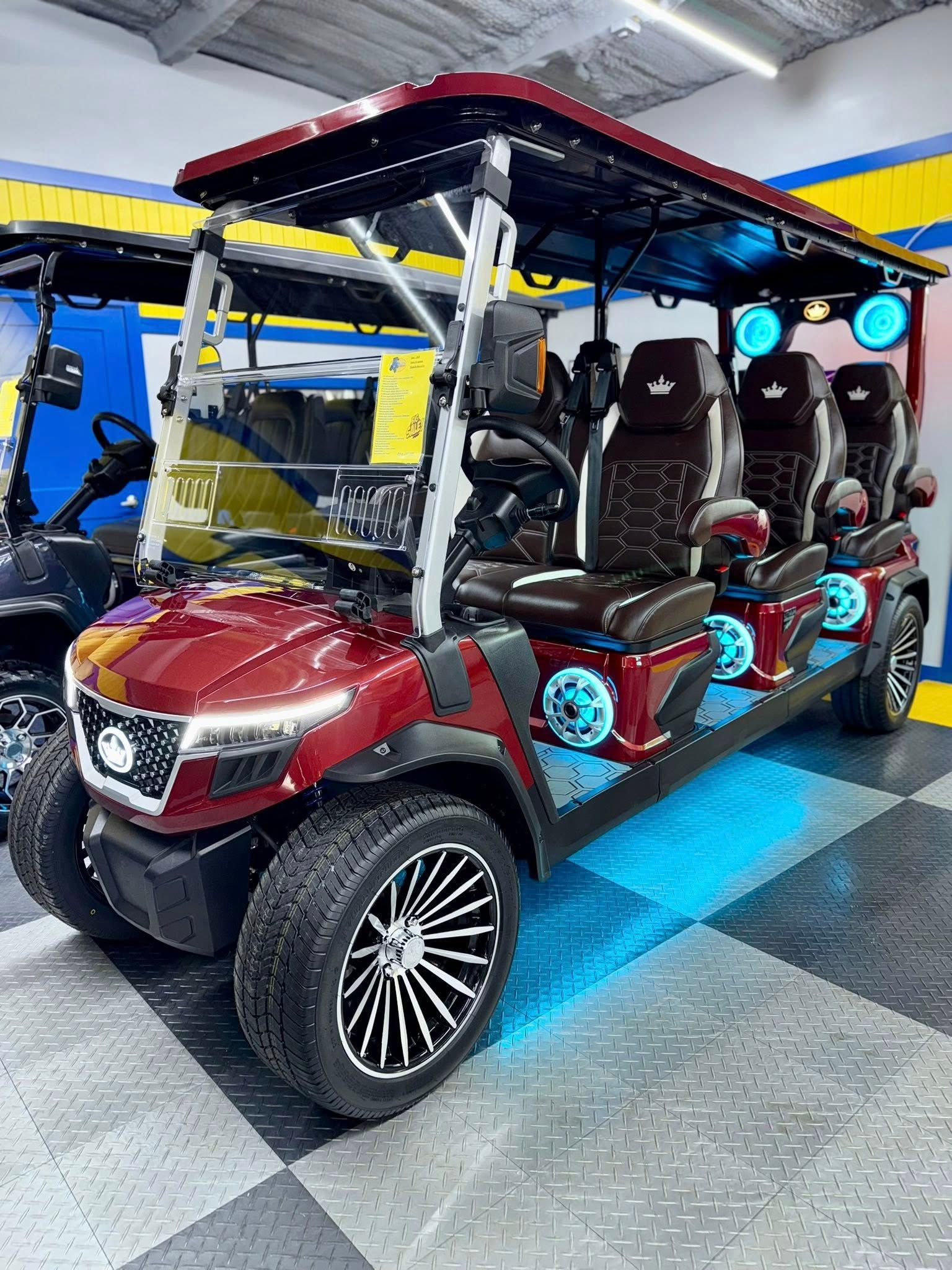 Red golf cart with custom black and white wheels, seating for six, and blue underglow lights.