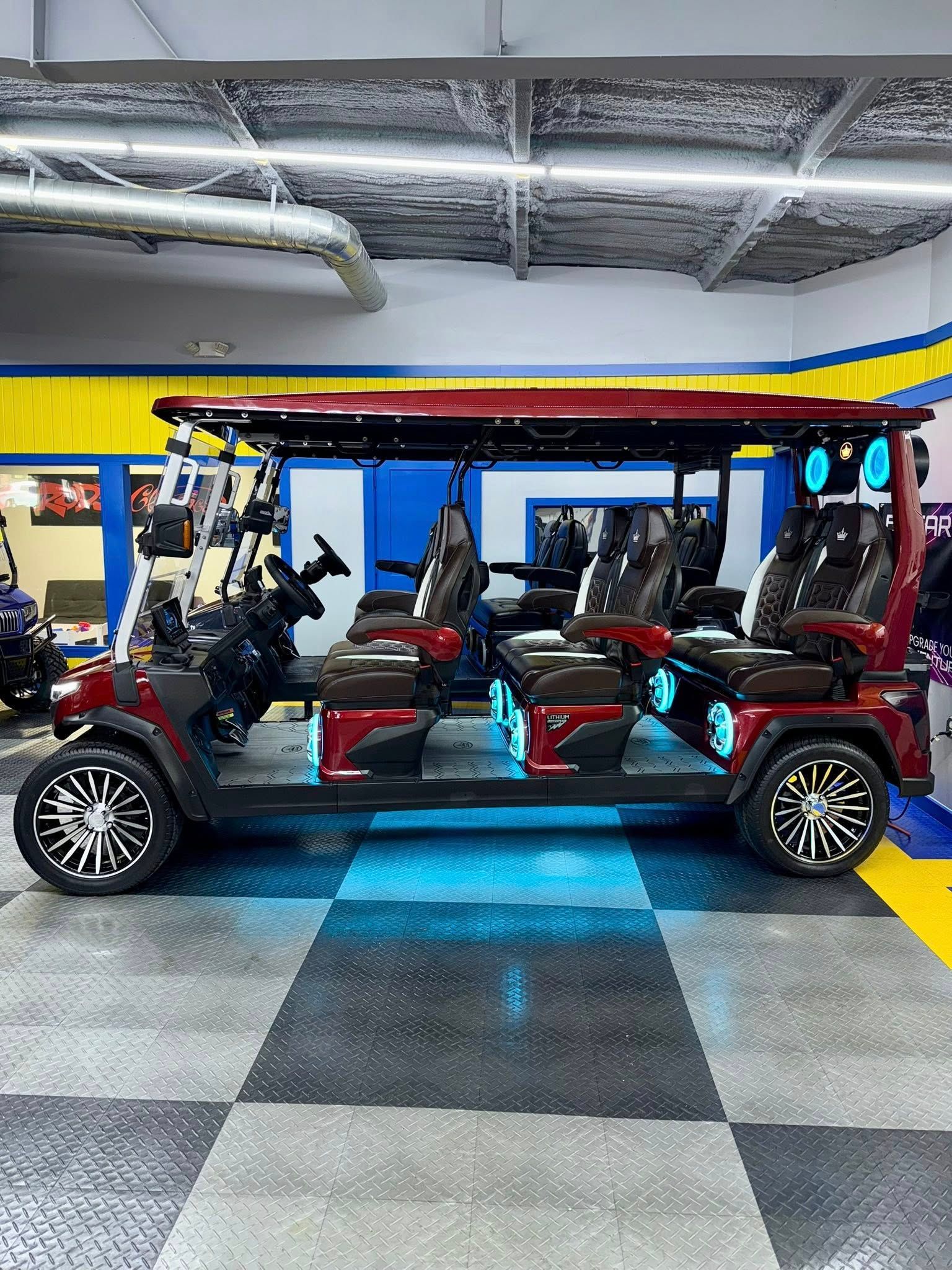 A red, 8-person golf cart with custom black and chrome wheels and blue under-glow lighting, parked inside a garage.