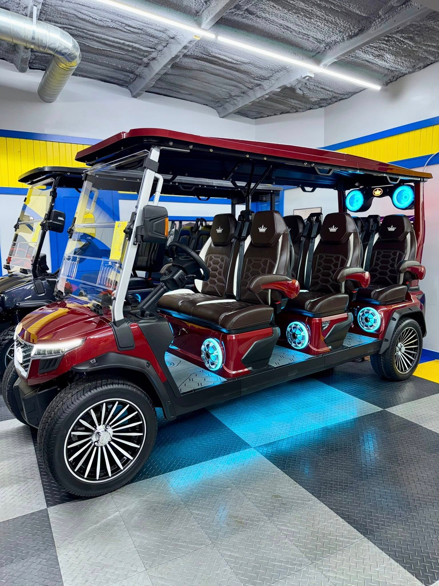 A burgundy, eight-seater golf cart with black and white rims, displayed inside a garage.
