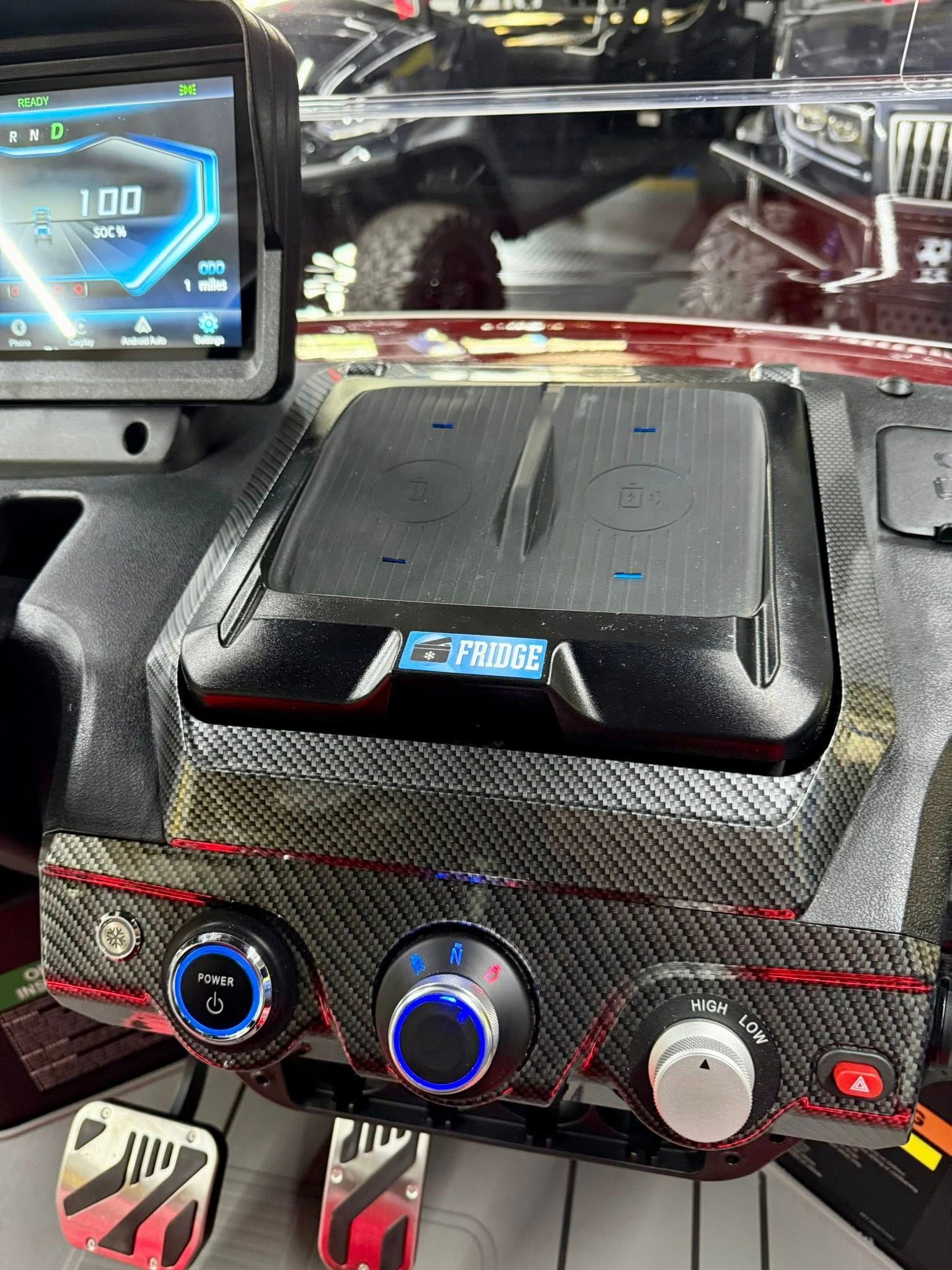 Interior of a custom vehicle dashboard with a touchscreen display, air vents, and control knobs, featuring carbon fiber accents and red trim.