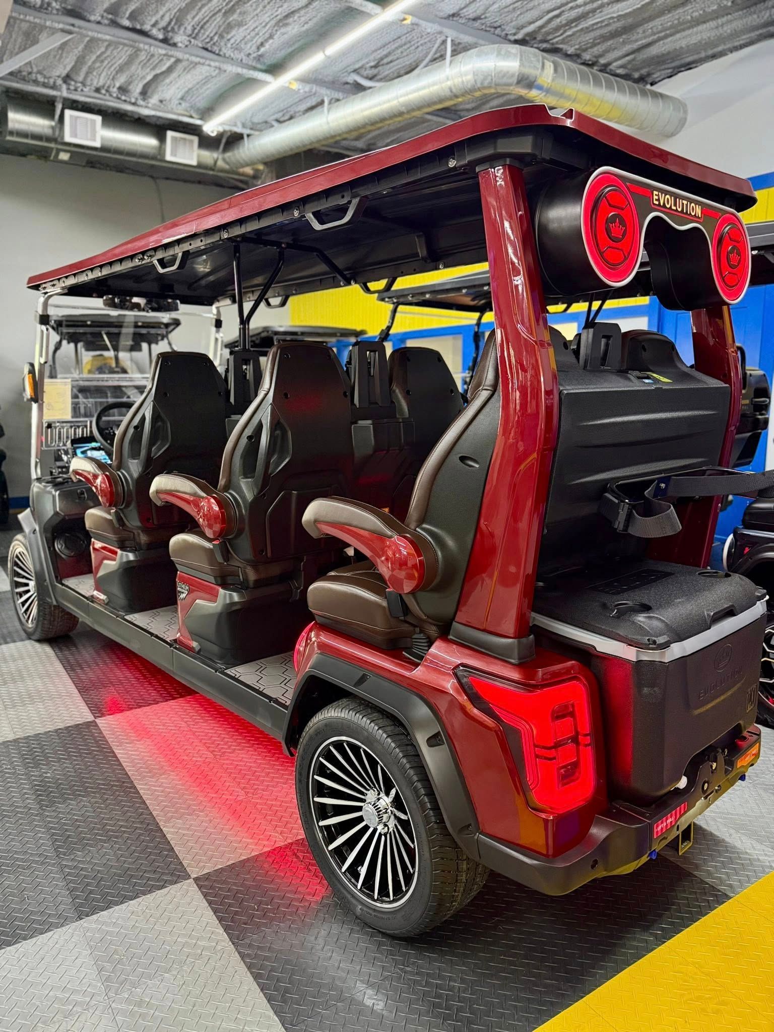 Red and black golf cart with eight seats and a rooftop speaker system, parked indoors with red under-glow lighting.