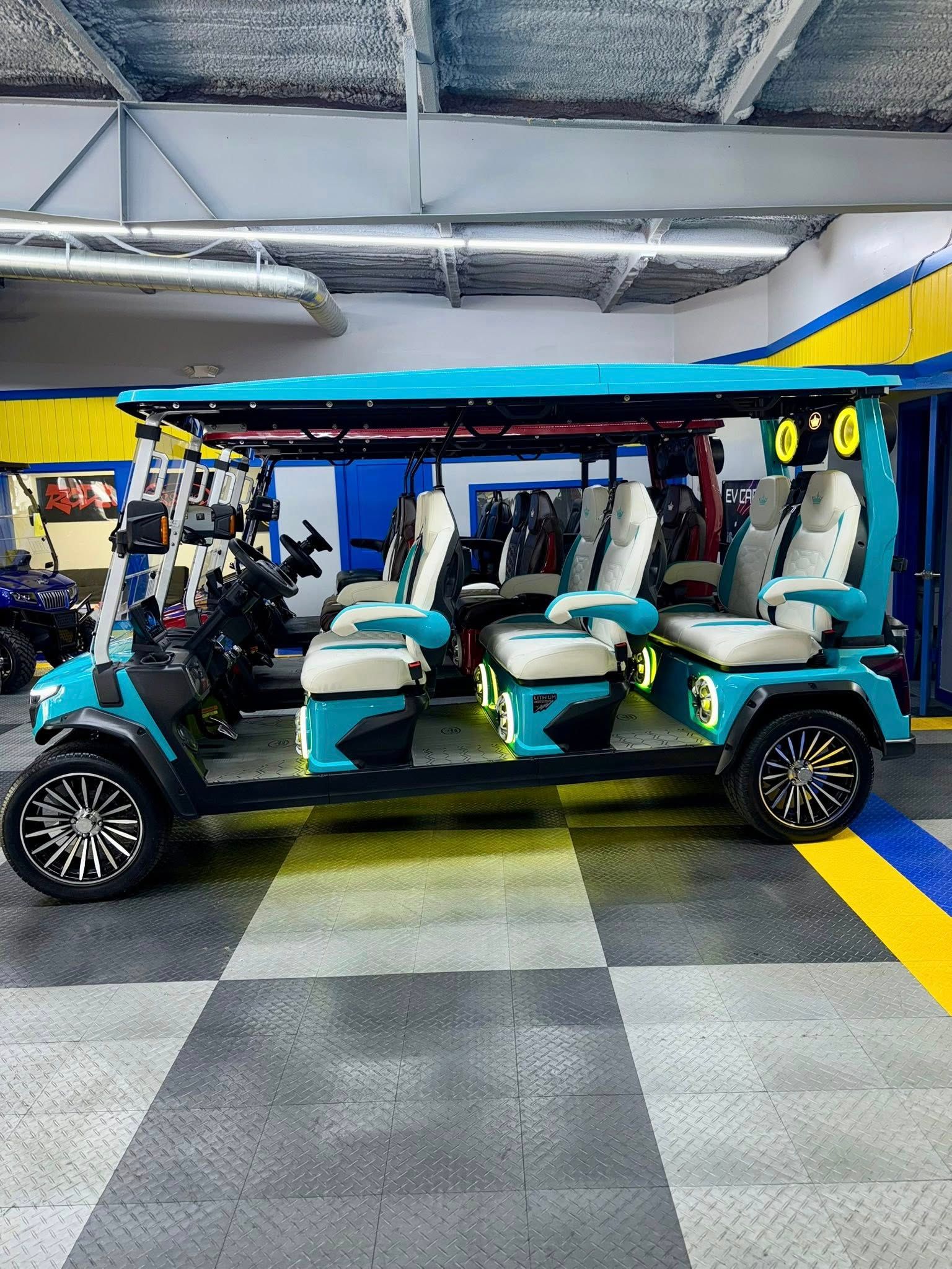 A teal six-seater golf cart with white and beige seats. It has black wheels and is indoors on a checkered floor.