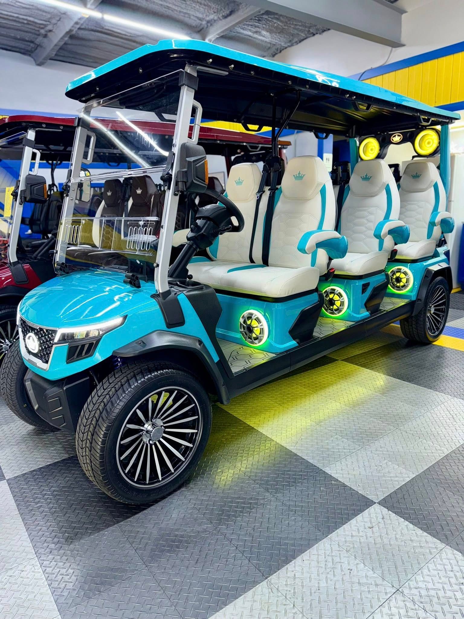A customized, turquoise golf cart with white and turquoise seats, black rims, and illuminated features is parked in a showroom.