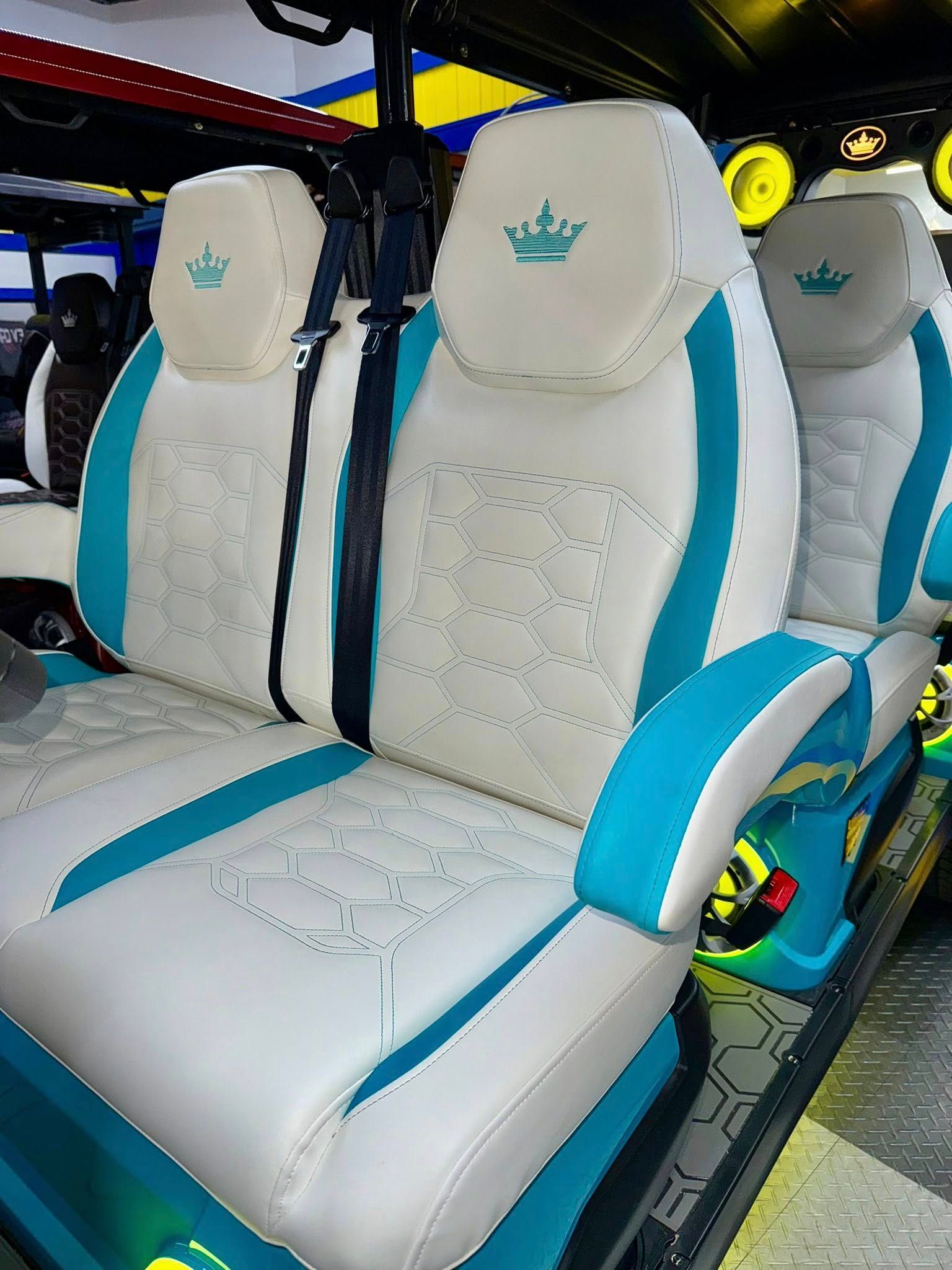 Golf cart seats with white and turquoise upholstery, featuring a crown emblem on headrests.