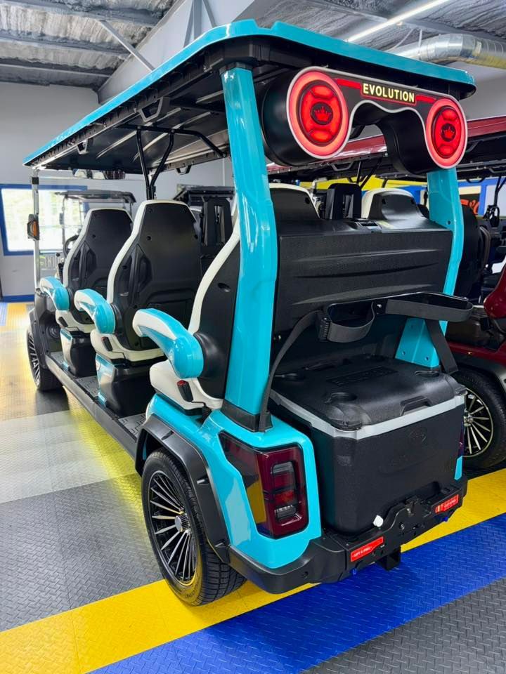 A blue and black Evolution golf cart, with seating for many, in a showroom setting.  It has large taillights and a cooler on the back.