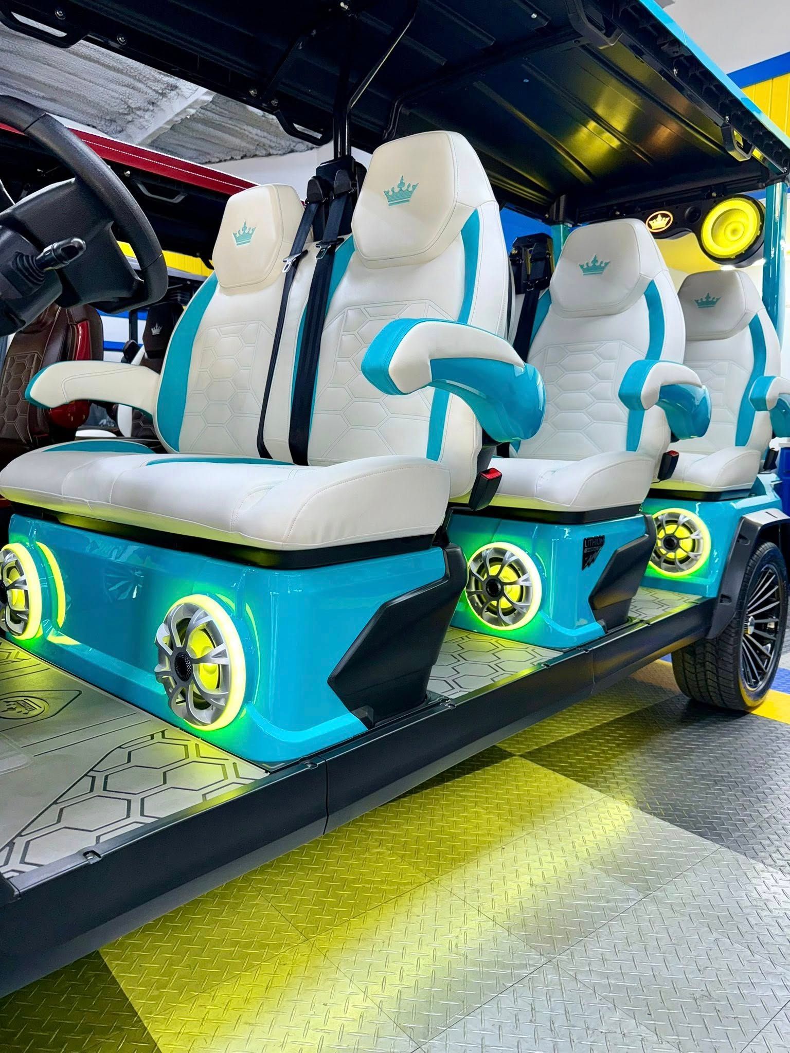 A golf cart with white and teal seating. The cart is illuminated with blue and yellow lights.