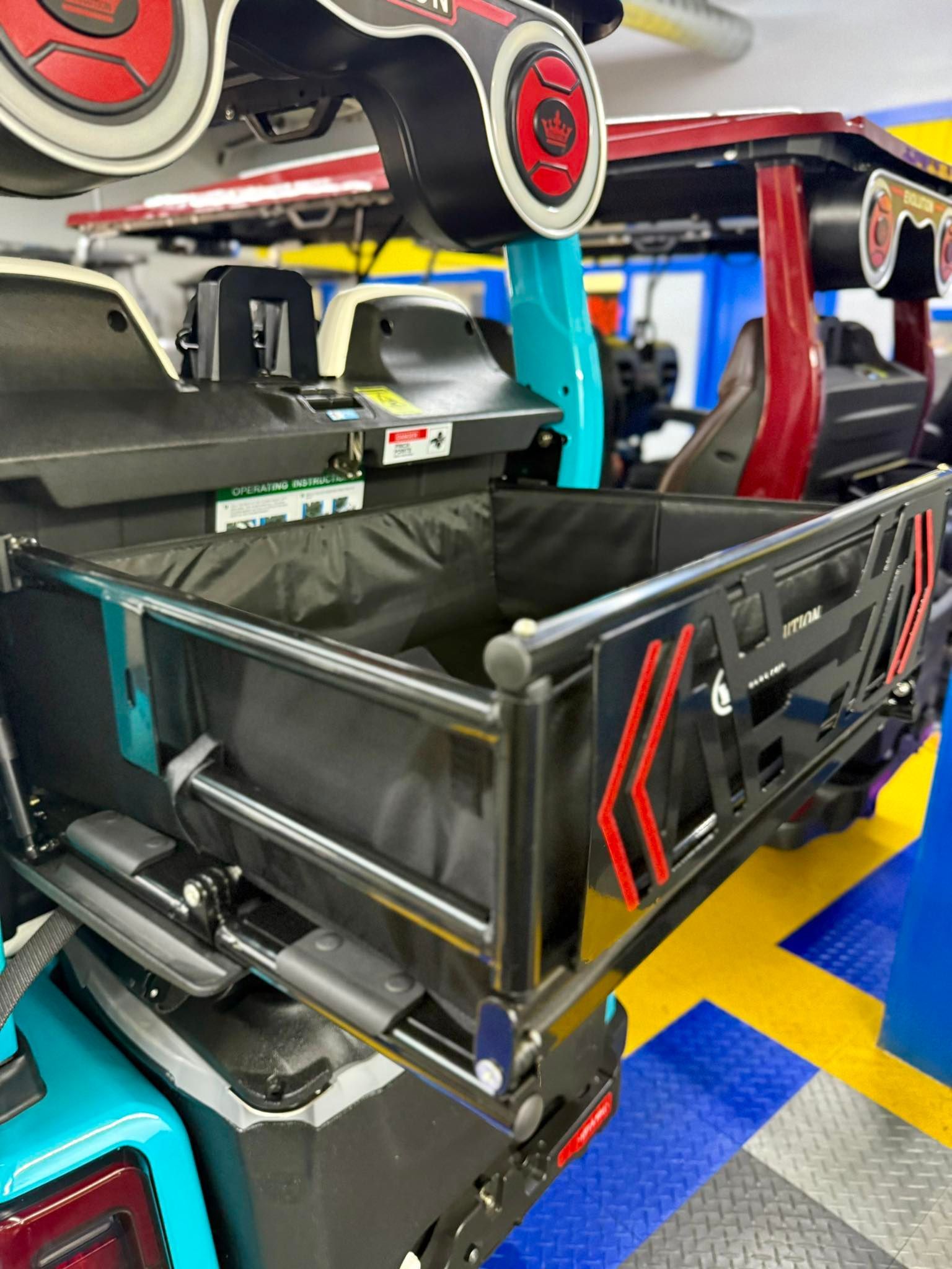 A black cargo carrier on a teal and red off-road vehicle, open in a garage with a colorful floor.