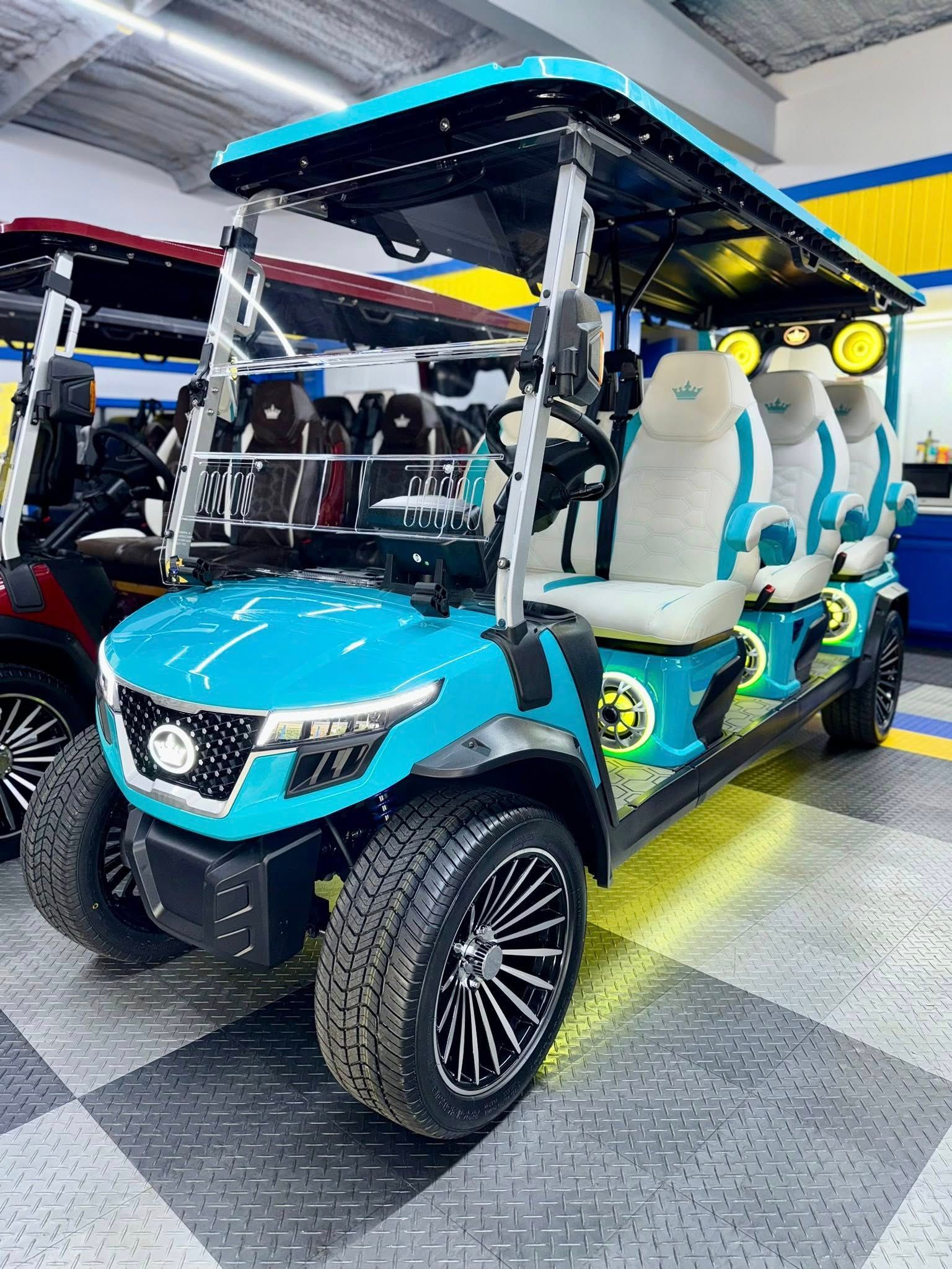 A custom turquoise golf cart with white and teal seats is parked indoors, featuring large wheels and bright lights.