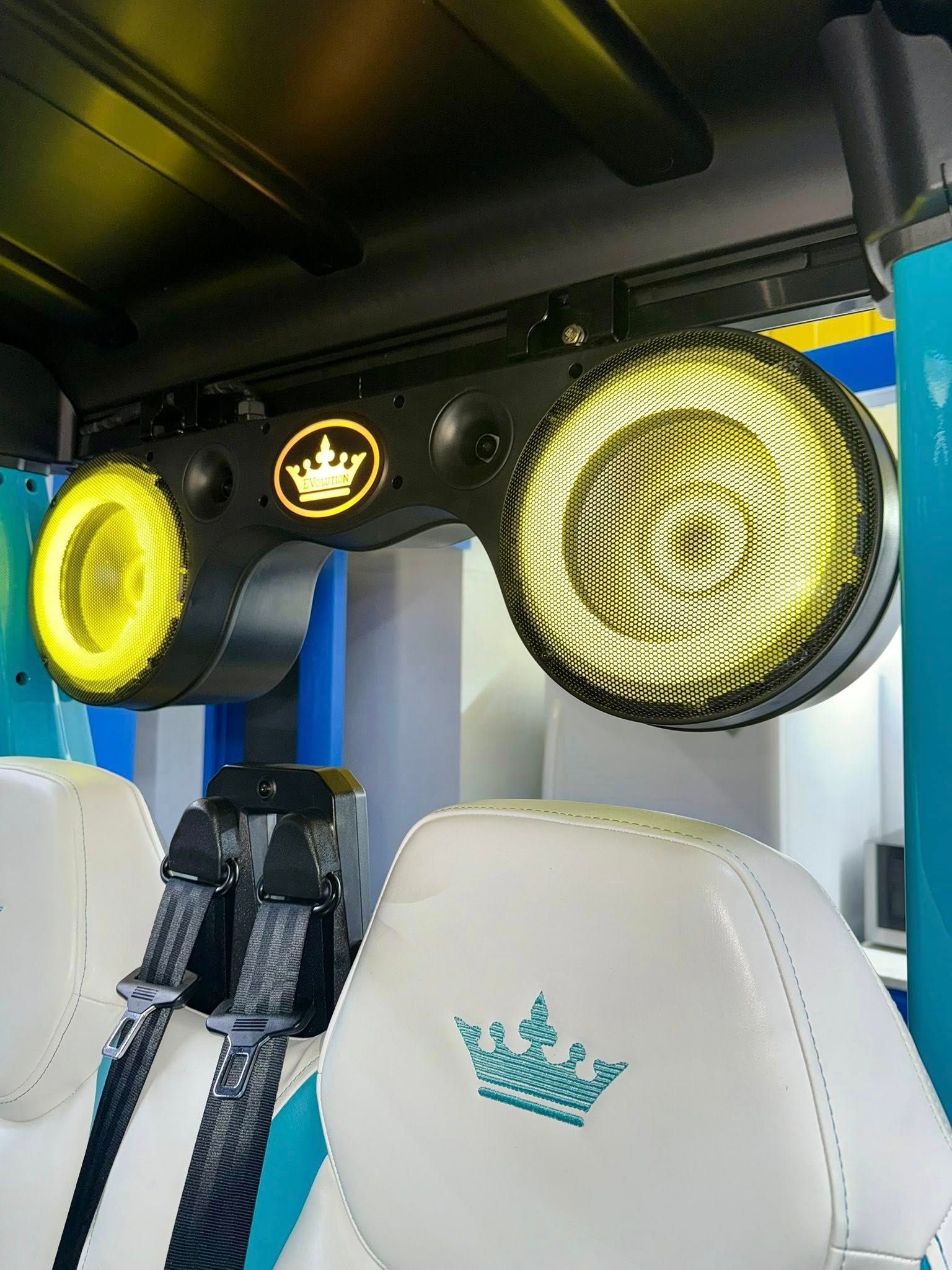 Interior of a golf cart with white seats and yellow accent lighting on a black overhead speaker bar. A crown logo is visible.