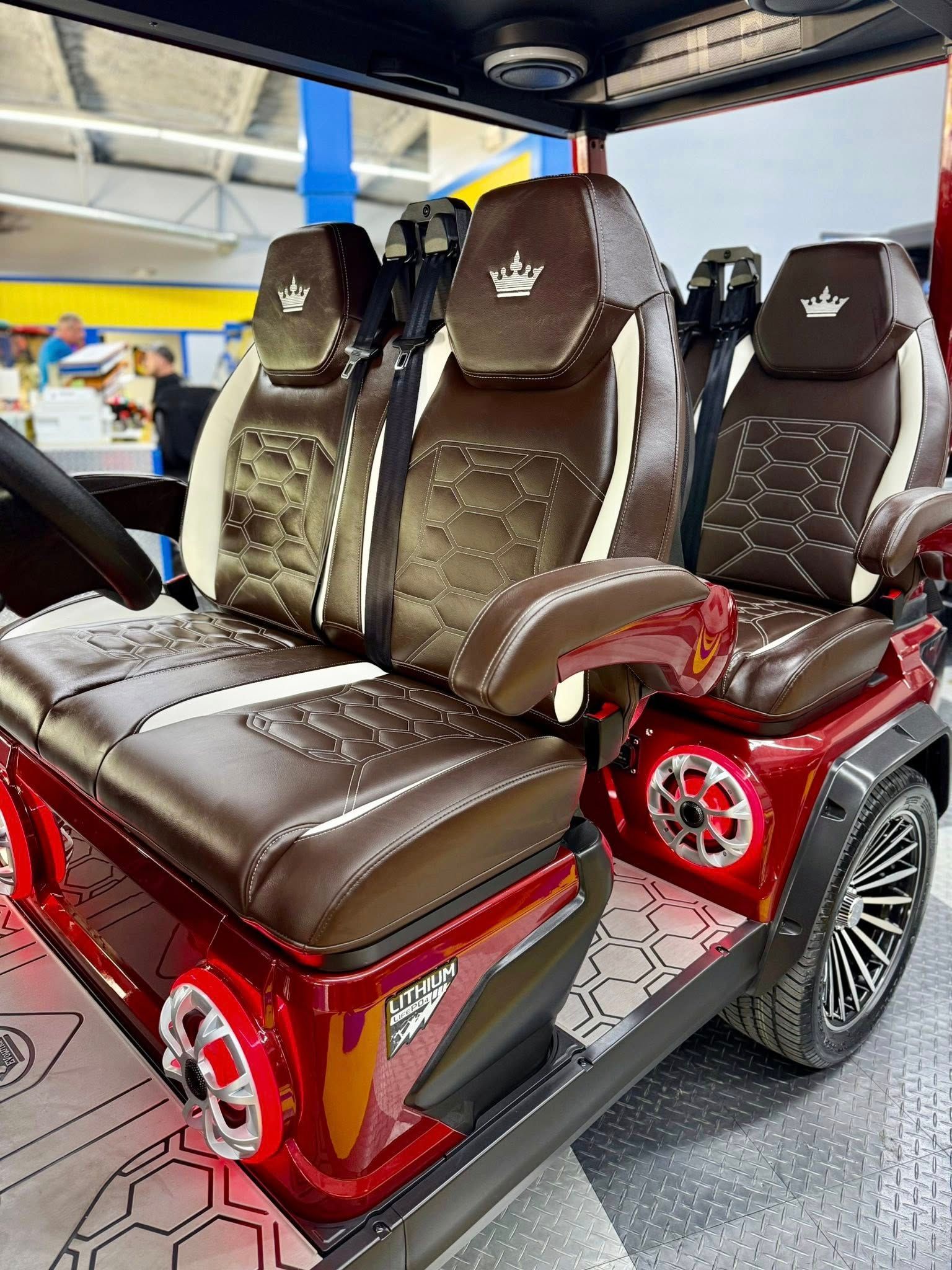 A red golf cart with brown leather seats and a crown on the back seat.