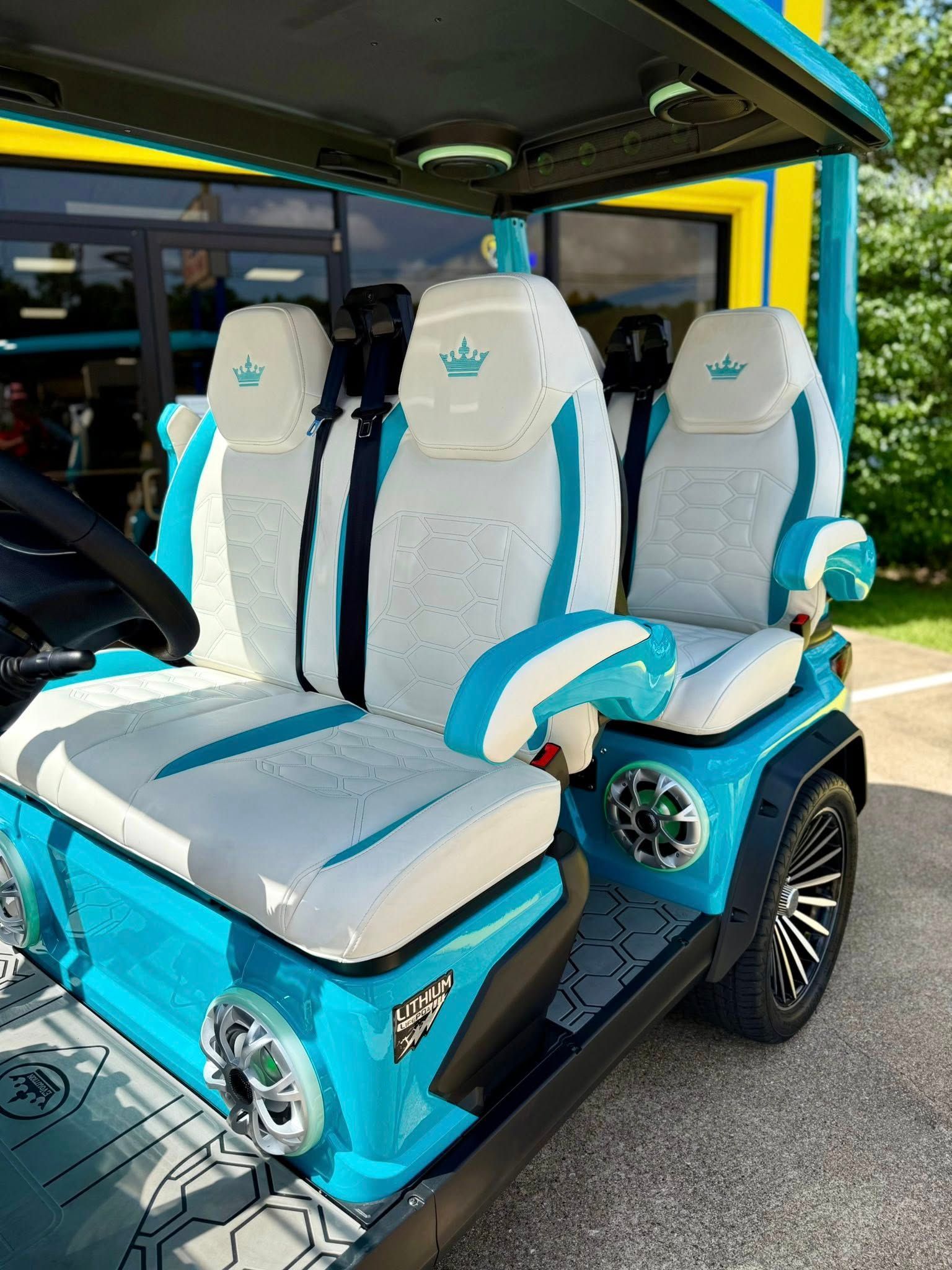 A blue and white golf cart with a crown on the seats is parked in a parking lot.