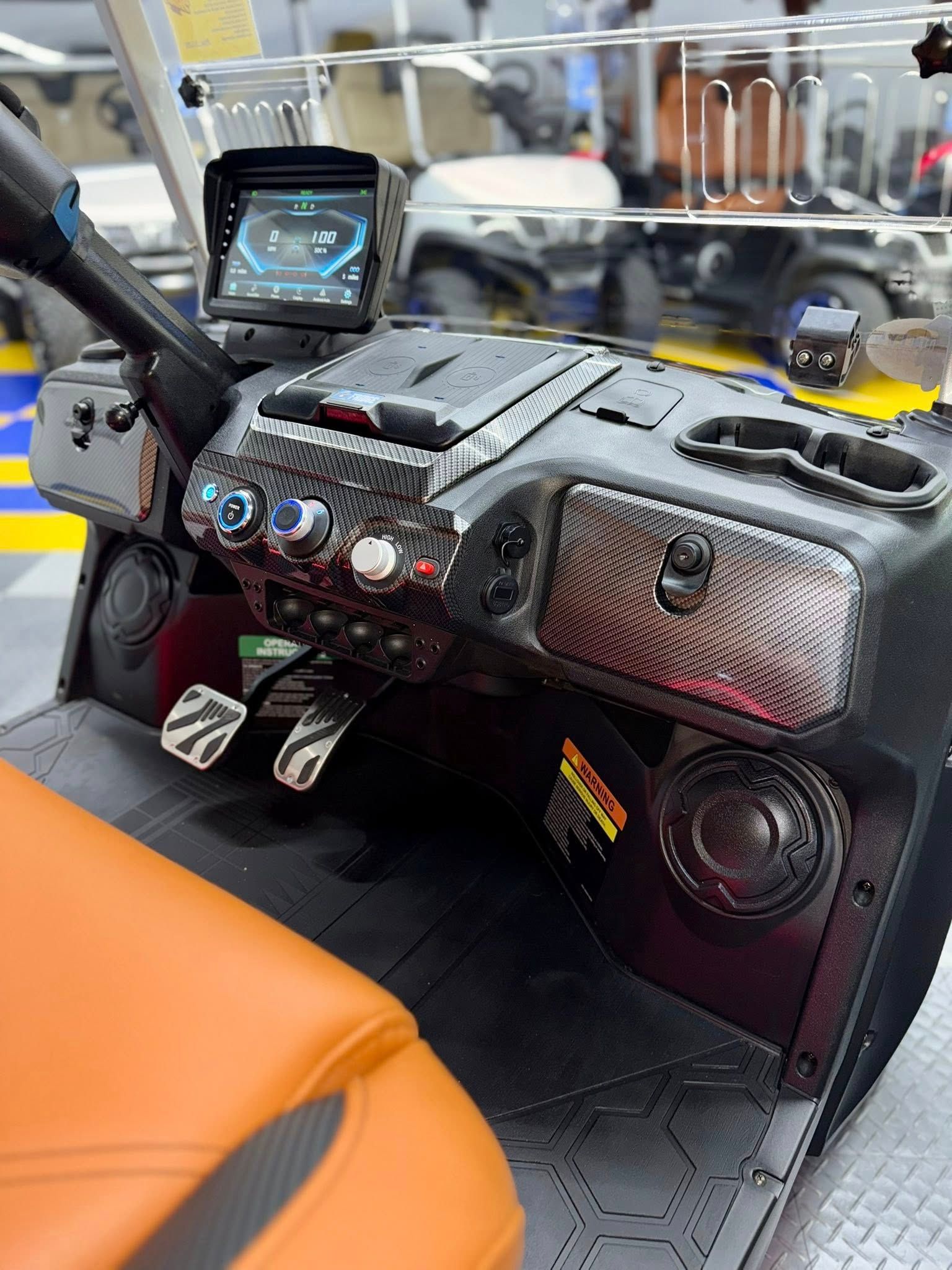 Interior of a black and brown golf cart; console with display, speakers, and carbon fiber accents.