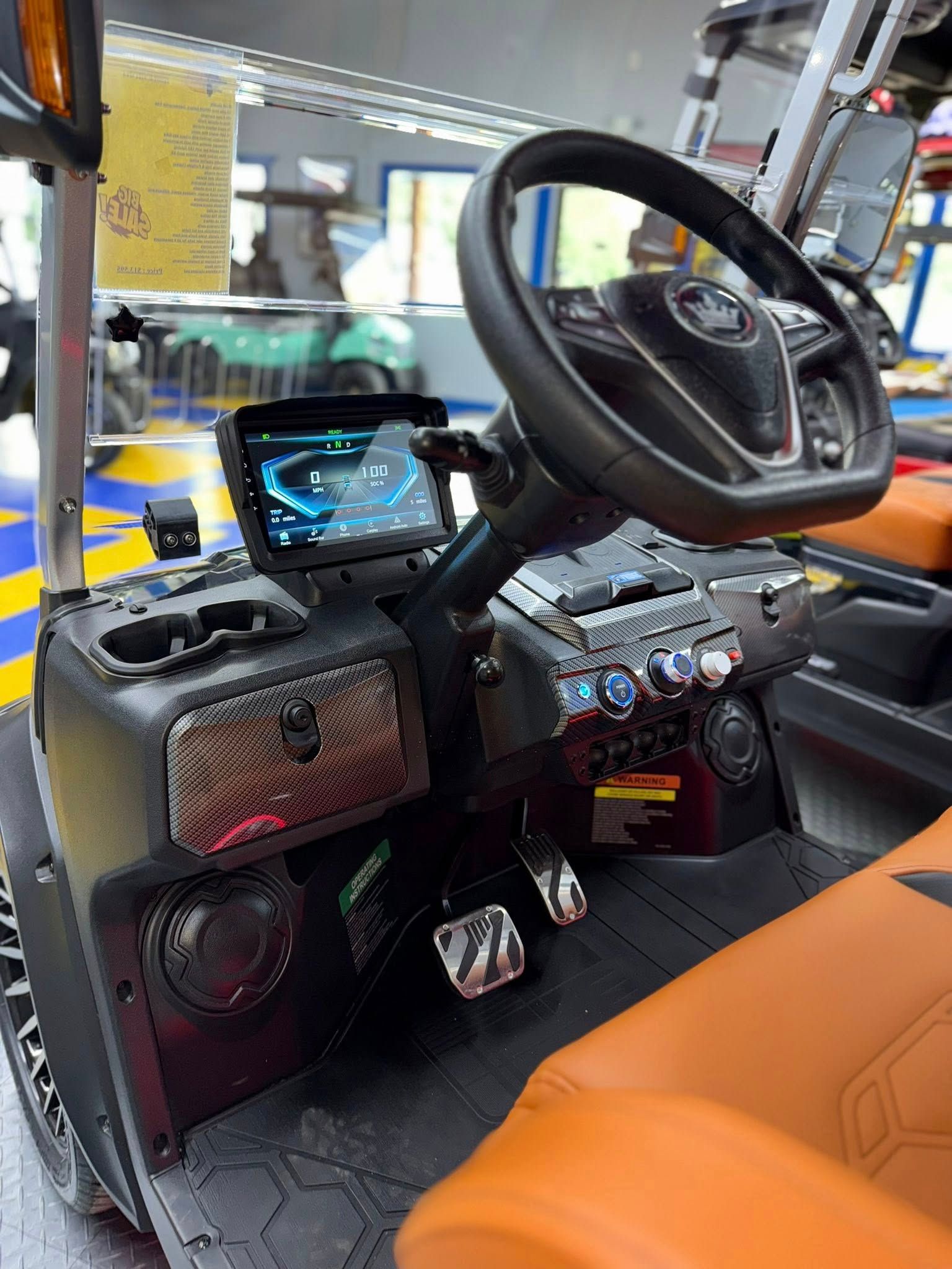 Golf cart interior with black dashboard, touch screen, tan seats, and black steering wheel.