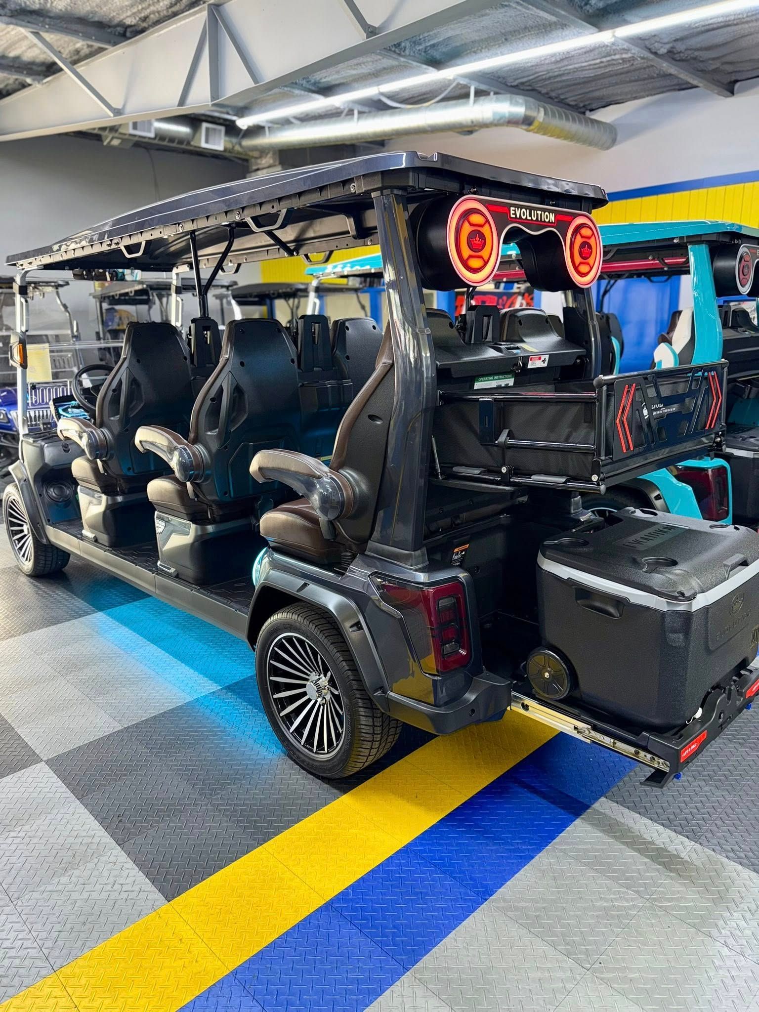 Black customized golf cart with multiple seats, speakers, and cooler inside a shop.