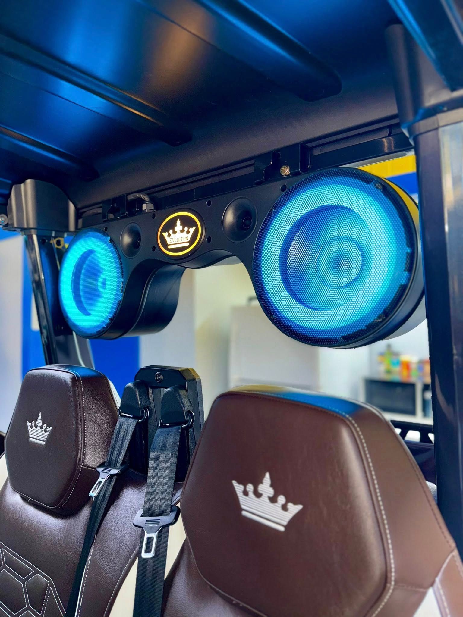 Interior of a vehicle with blue illuminated speakers above brown seats with crown emblems.