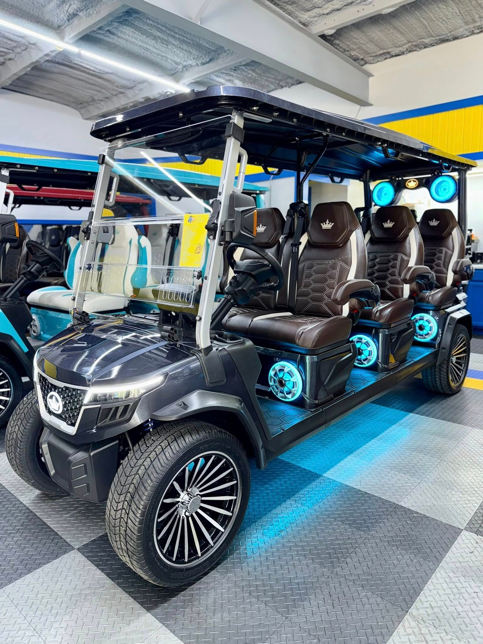Dark golf cart with custom seats, LED lights, and chrome wheels, indoors.
