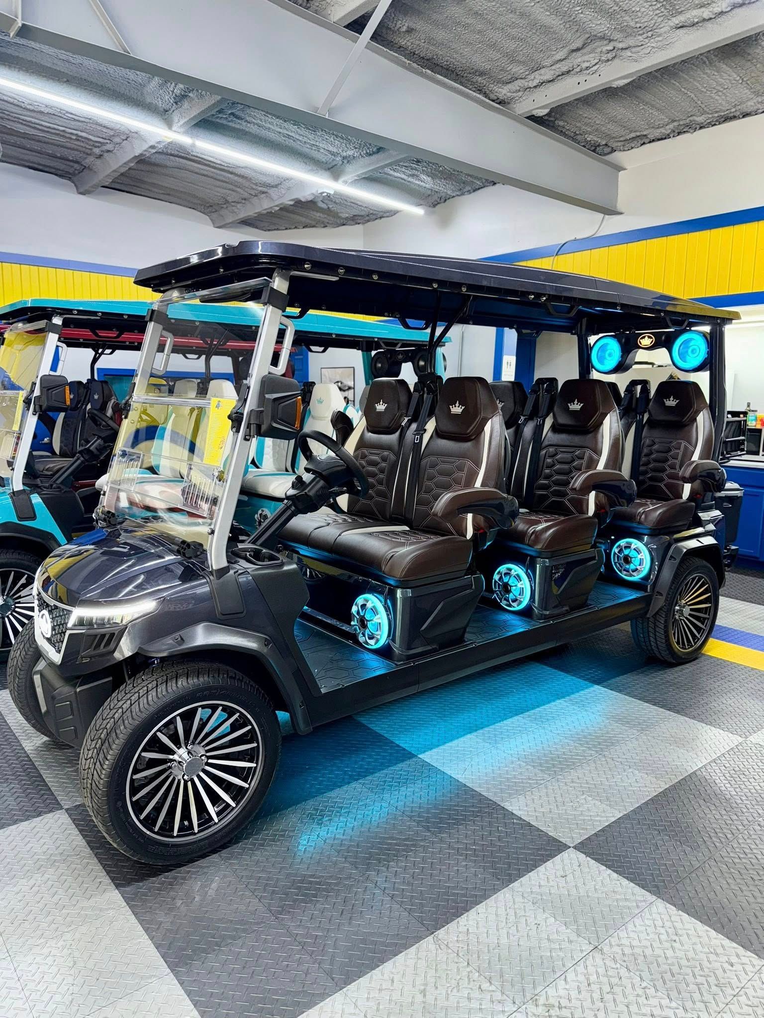 Dark gray, 6-person golf cart with black and brown leather seats, LED lights, and custom wheels, indoors.