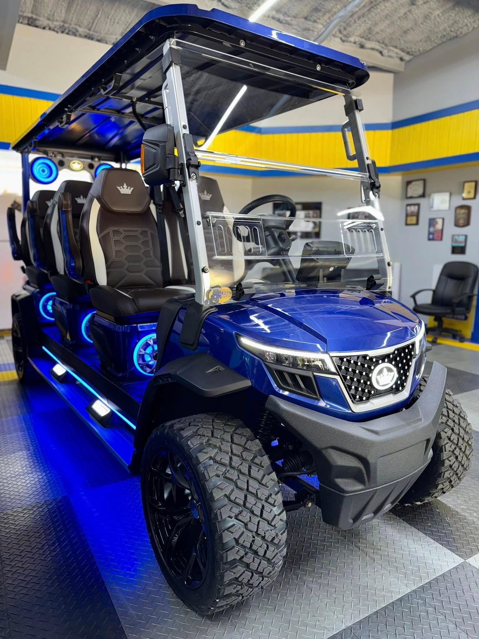 Blue custom golf cart with off-road tires, LED lighting, and black interior parked indoors.