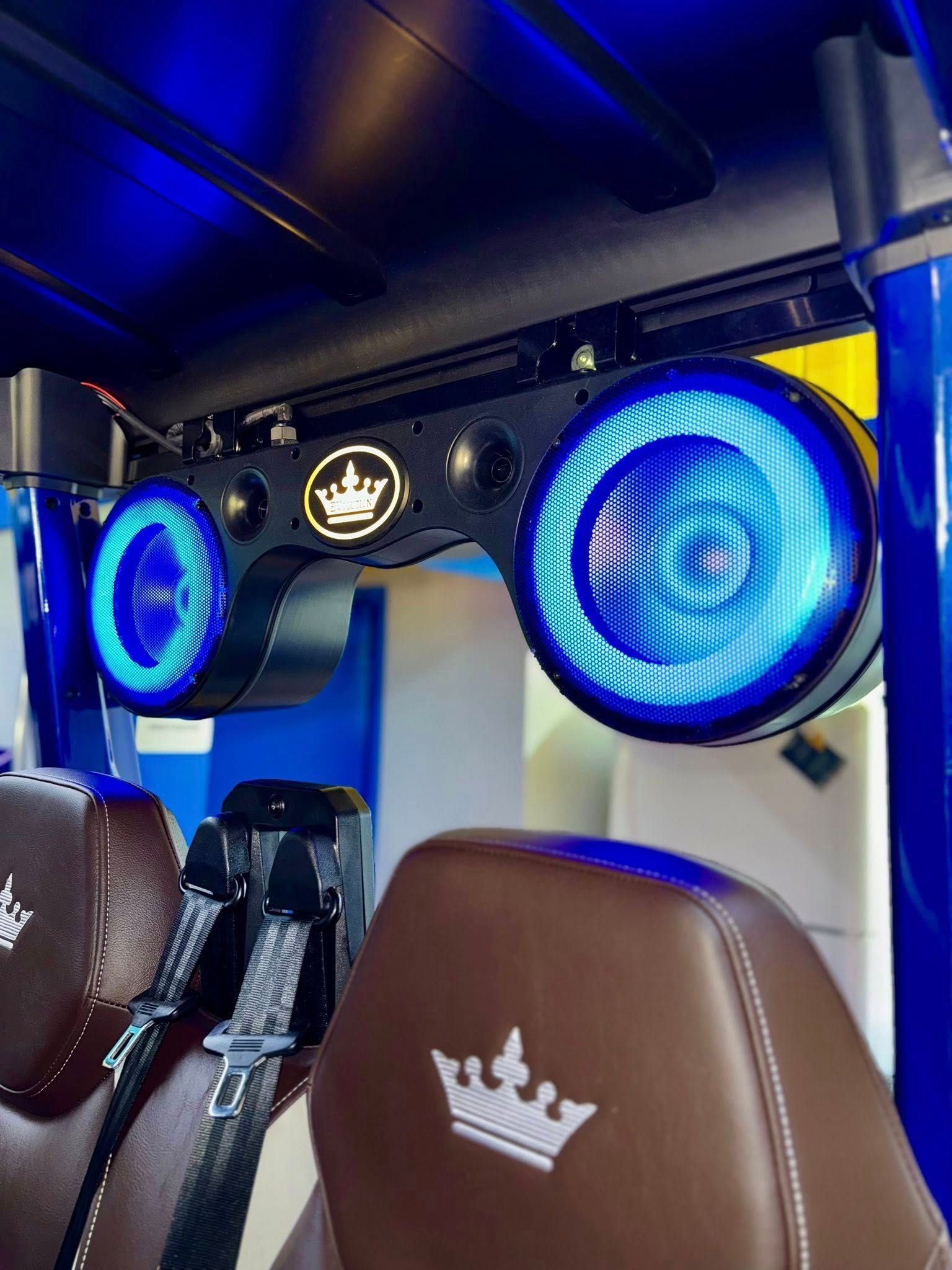 Blue lit speakers above brown seats with crown logo; interior of a vehicle.