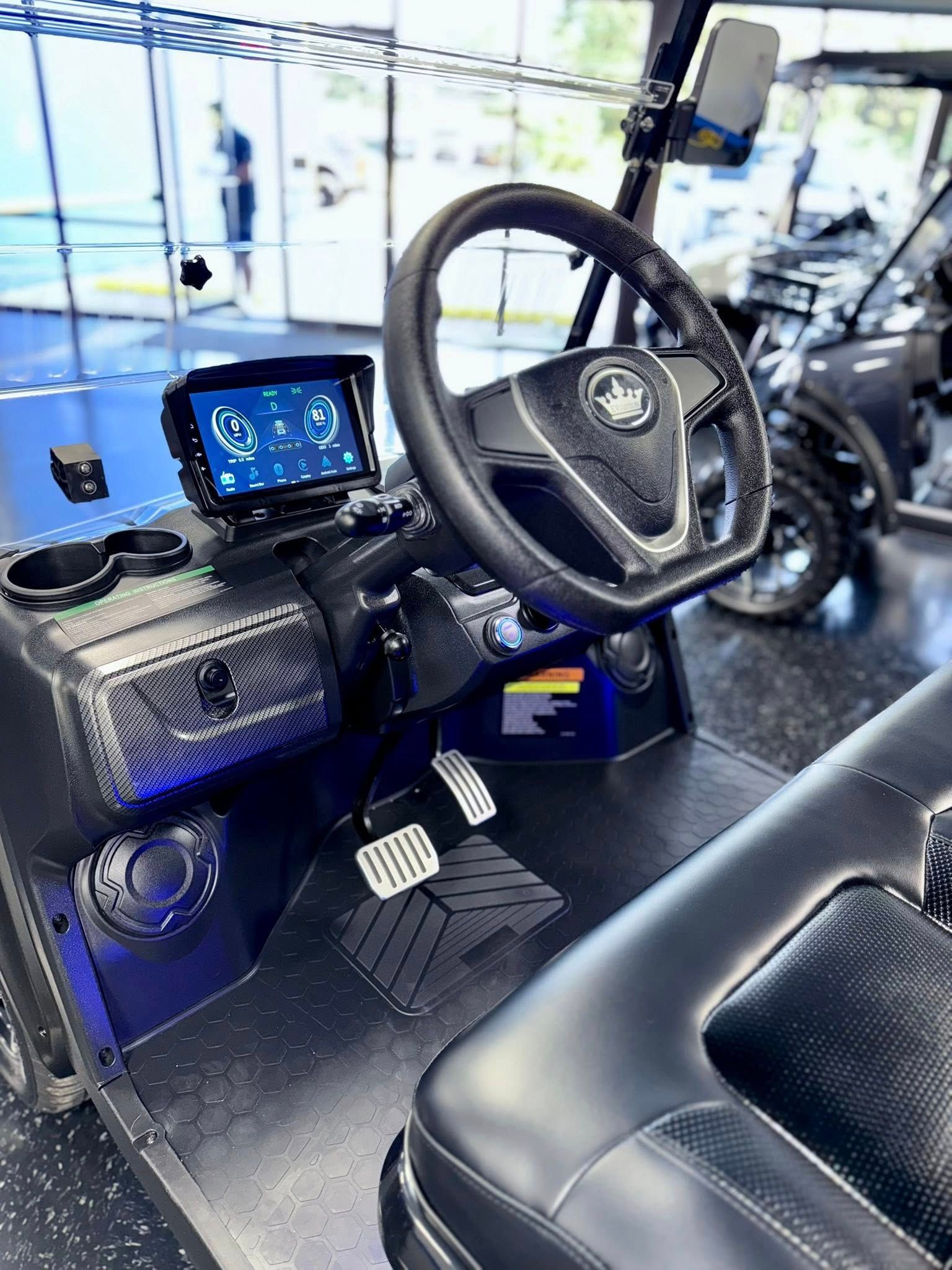 Interior of a black and blue golf cart with a digital dashboard, steering wheel, and pedals.
