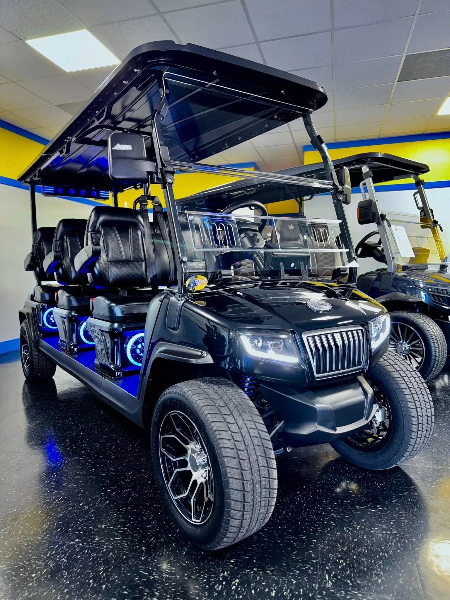 Black golf cart with blue LED lights, a Jeep-style grille, and black wheels, inside a showroom.