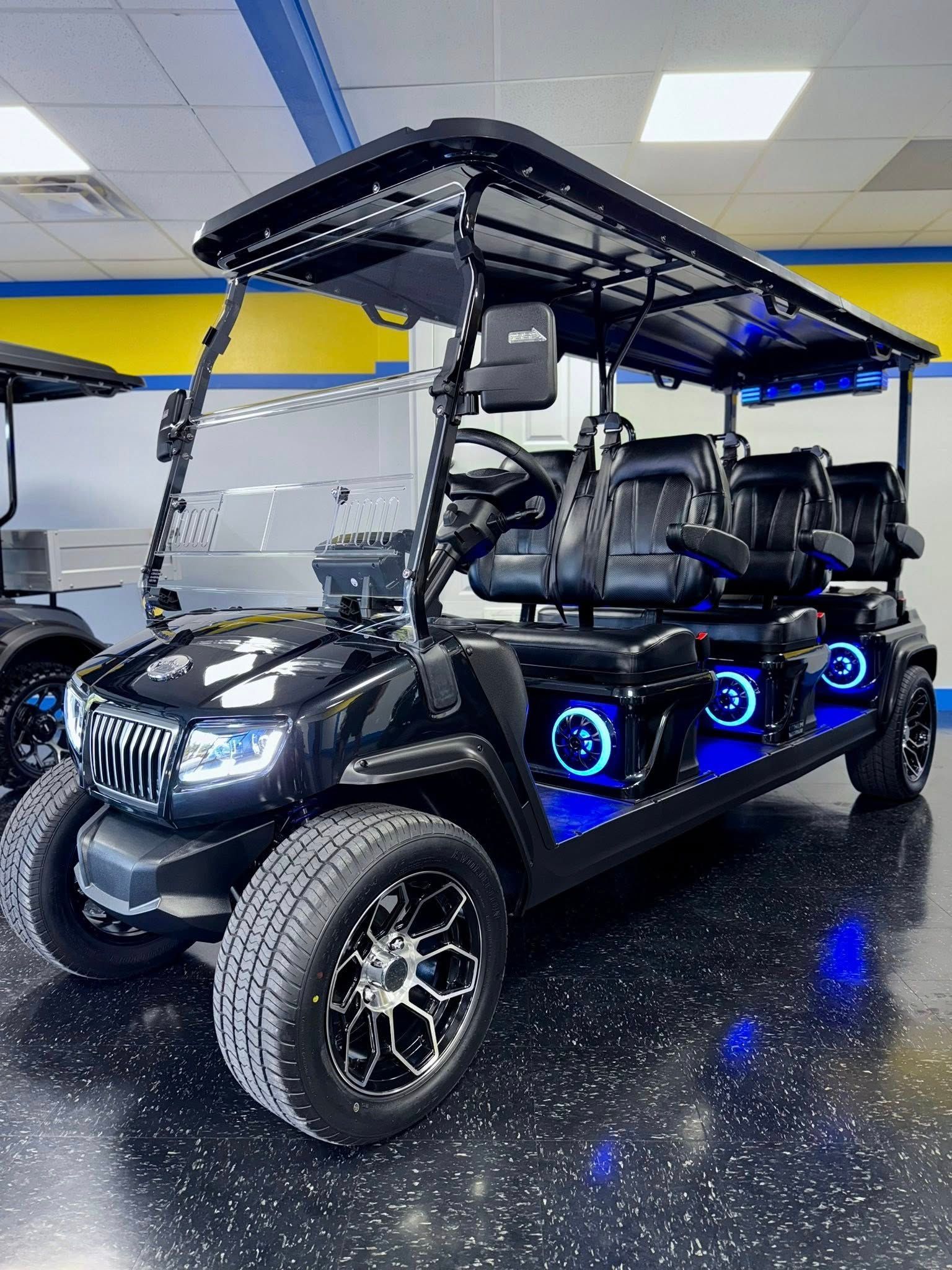 Black golf cart with blue underglow lights, off-road tires, and black seats. Interior setting.