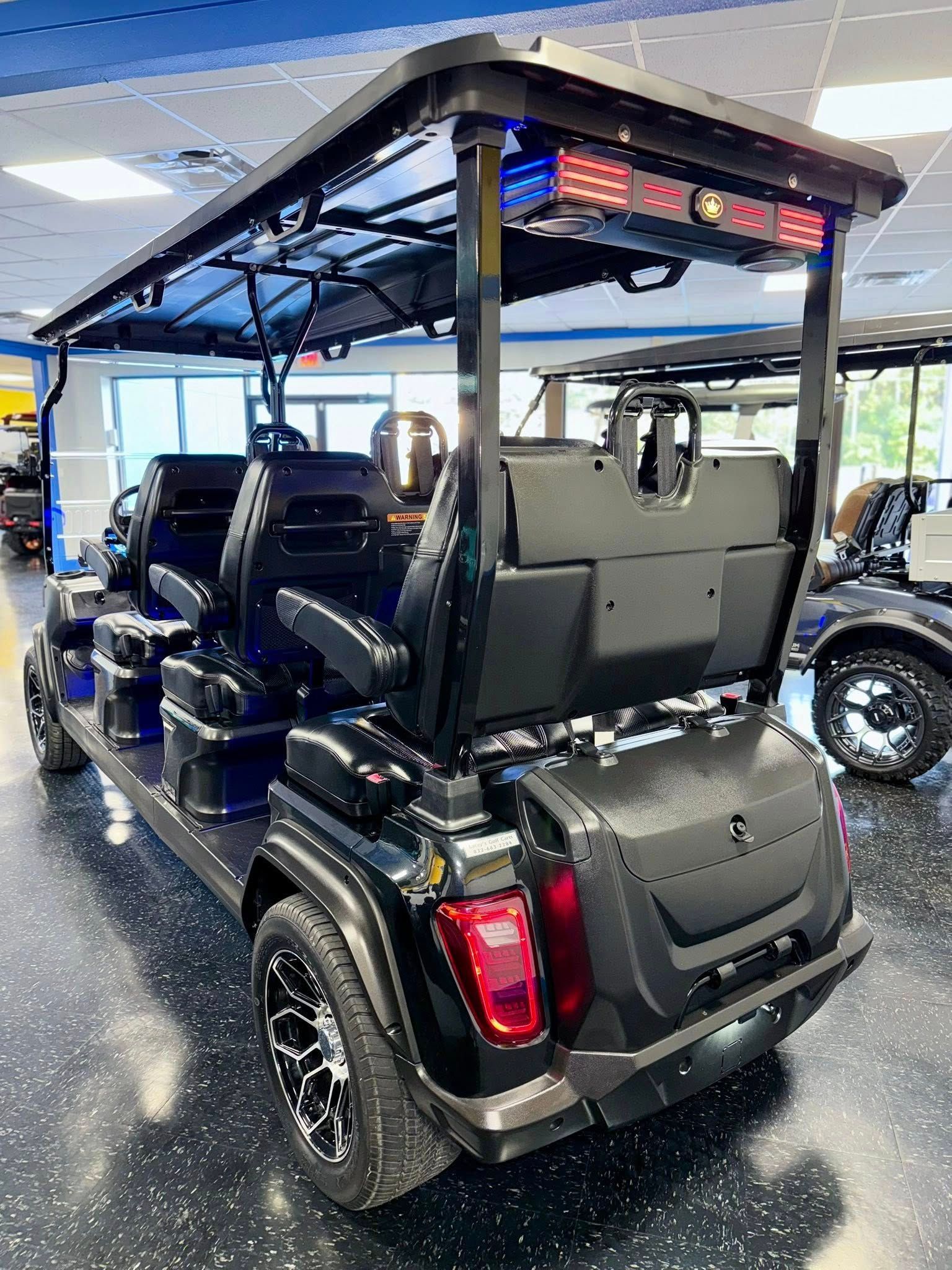 Black golf cart, six-seater, with black tires and roof. Tail lights visible.