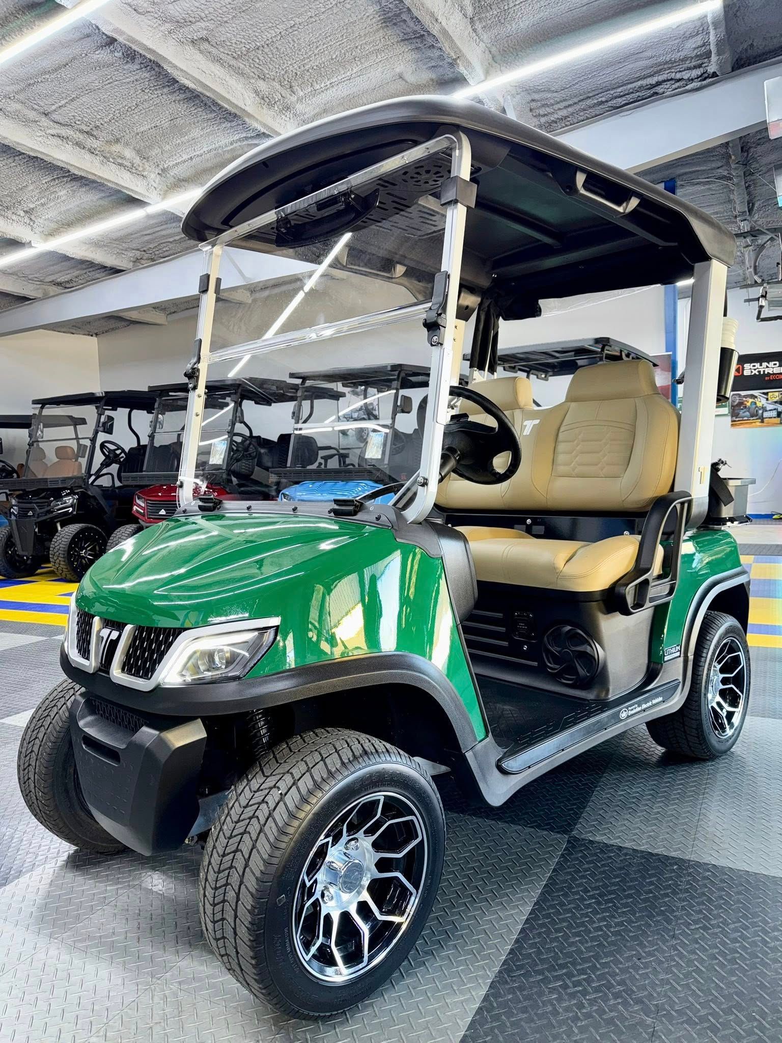 Green golf cart with tan seats and black roof, on a showroom floor.