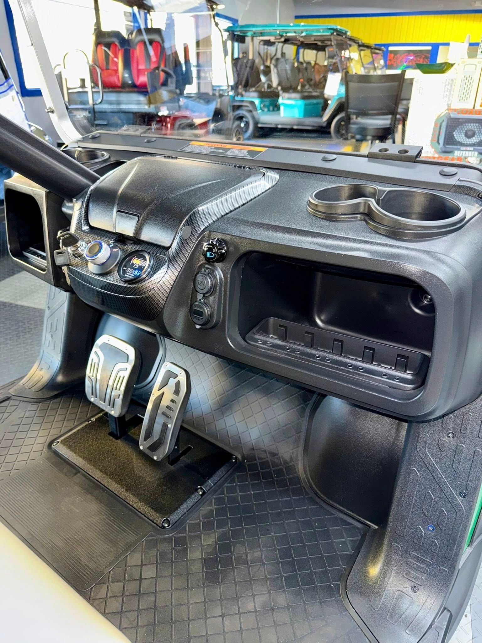 Dashboard of a golf cart with cup holders, storage, and pedals. Black and gray colors.
