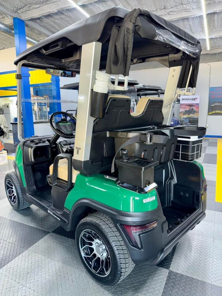 Green golf cart with black roof in a garage setting.