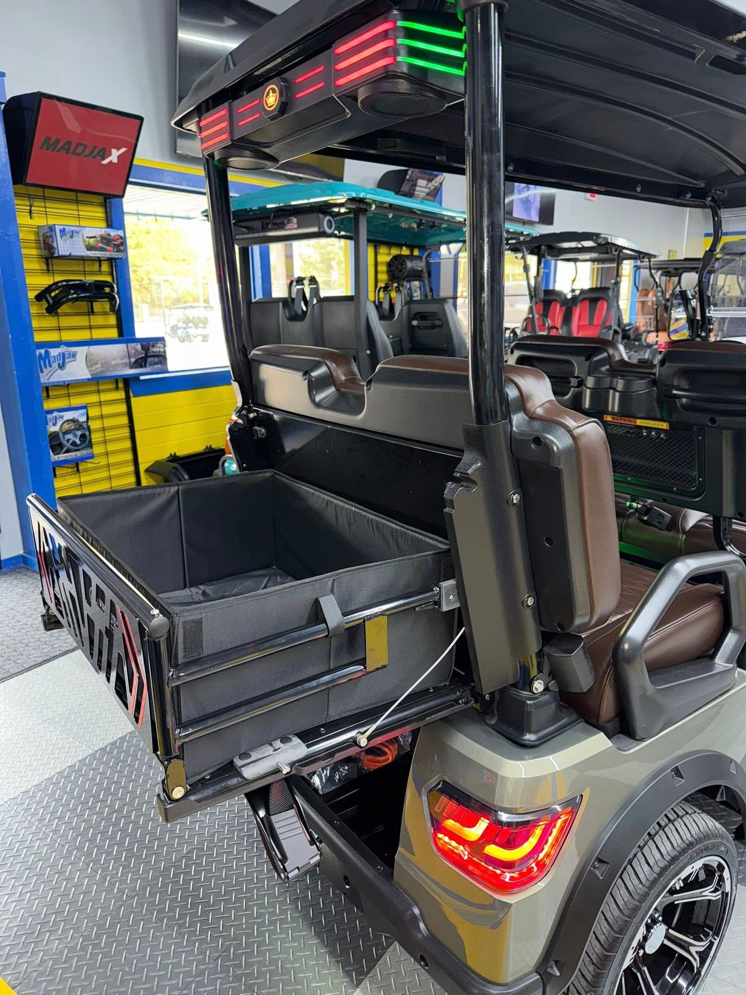 Golf cart with a pull-out cargo bed, brown and green accents, inside a showroom.