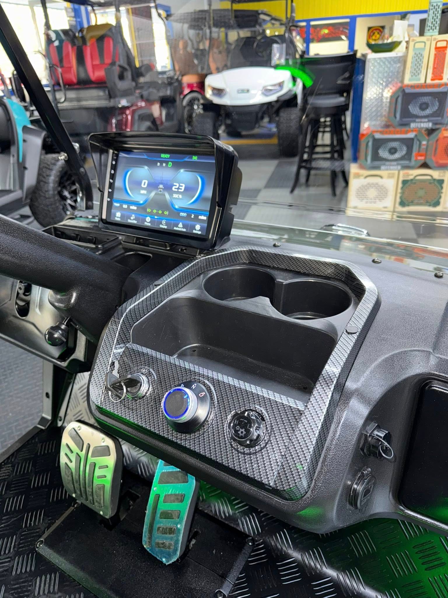 Golf cart dashboard with a large display, cup holders, and custom switches, in a shop.