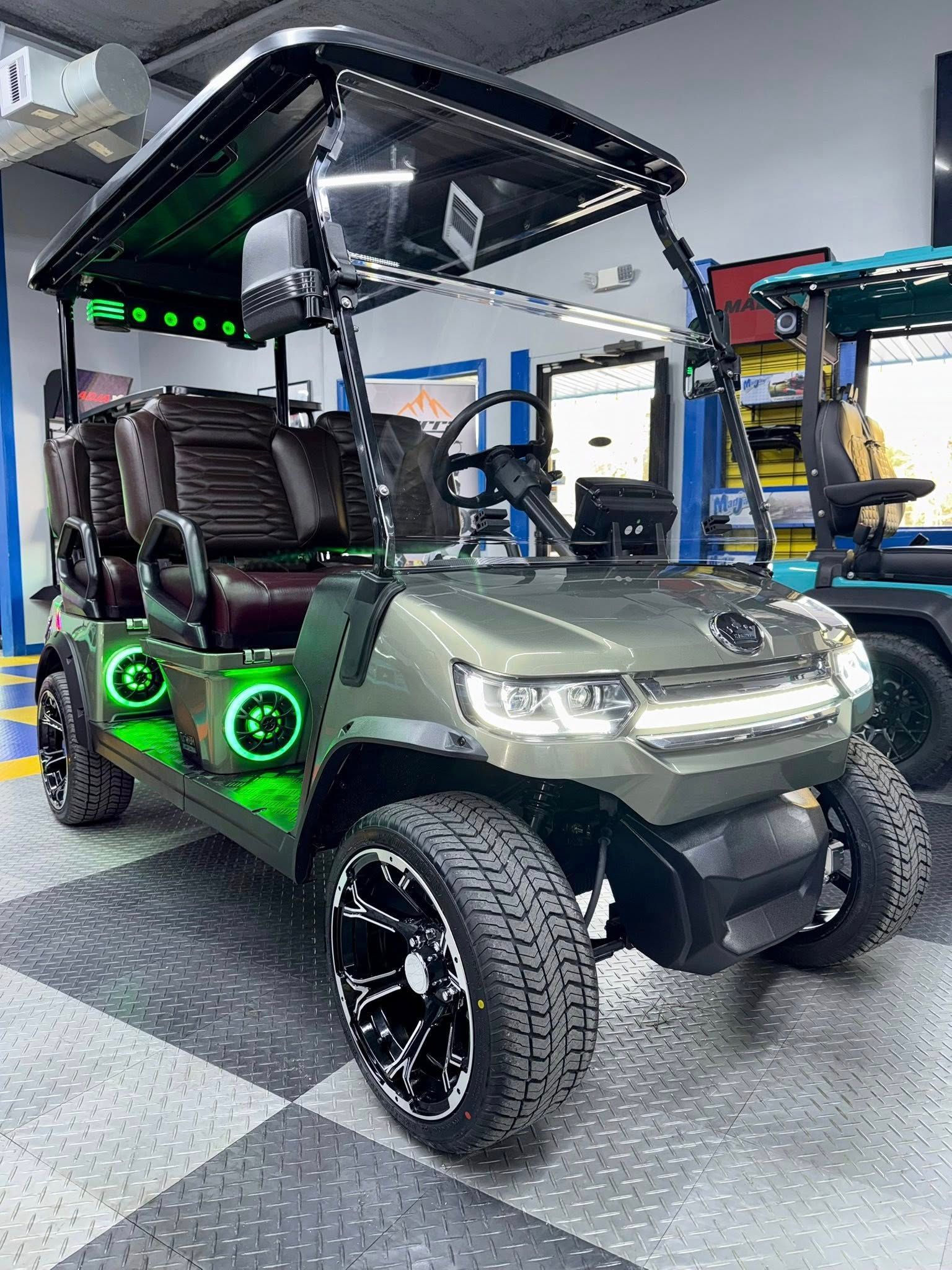 Olive green, customized golf cart with LED lights and black wheels, parked indoors.